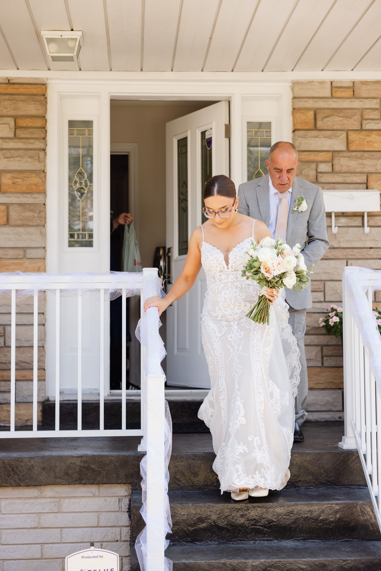 A wedding party exits through a stone-facade entrance decorated with white fabric.