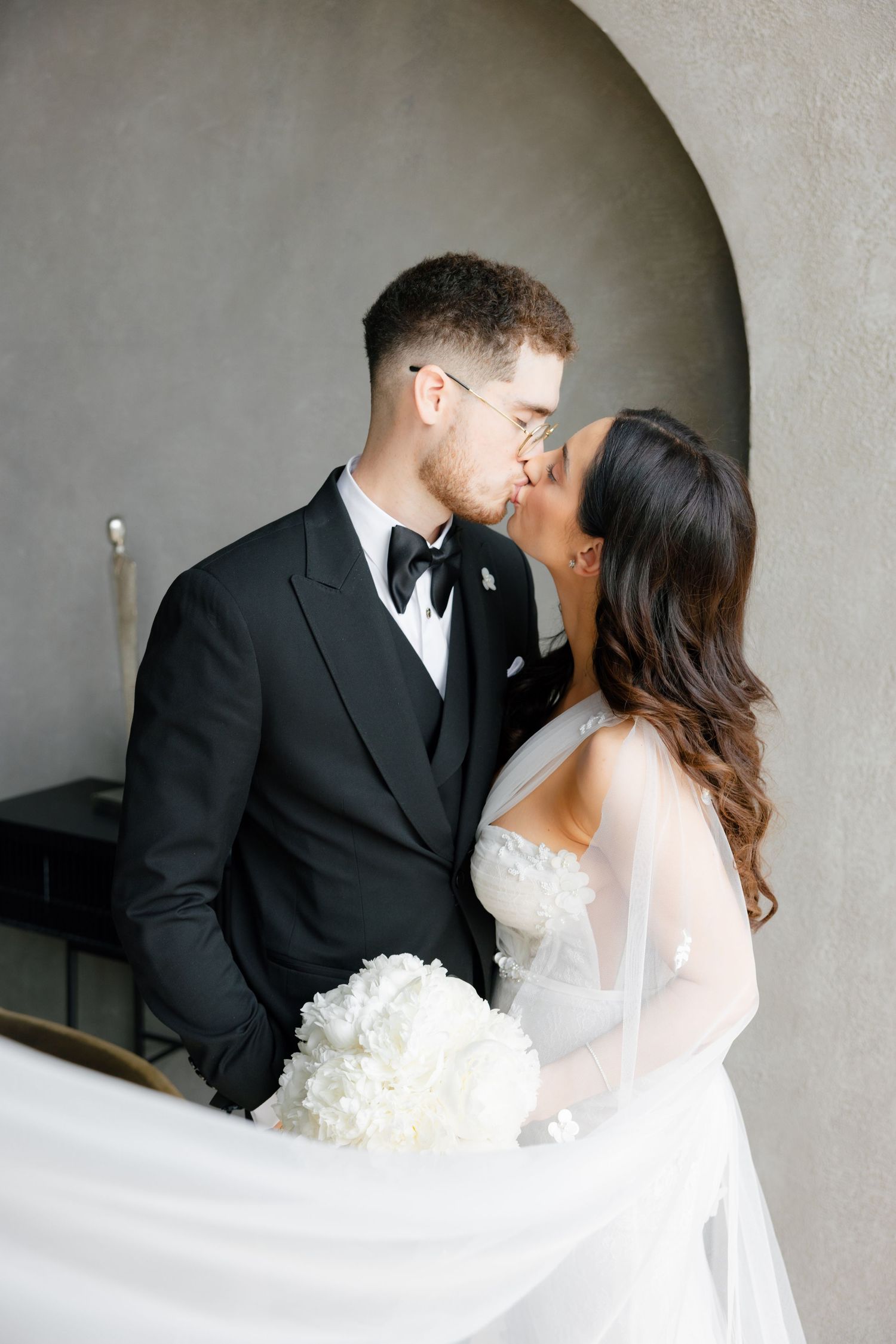 Intimate wedding portrait of couple sharing tender moment under concrete arch.