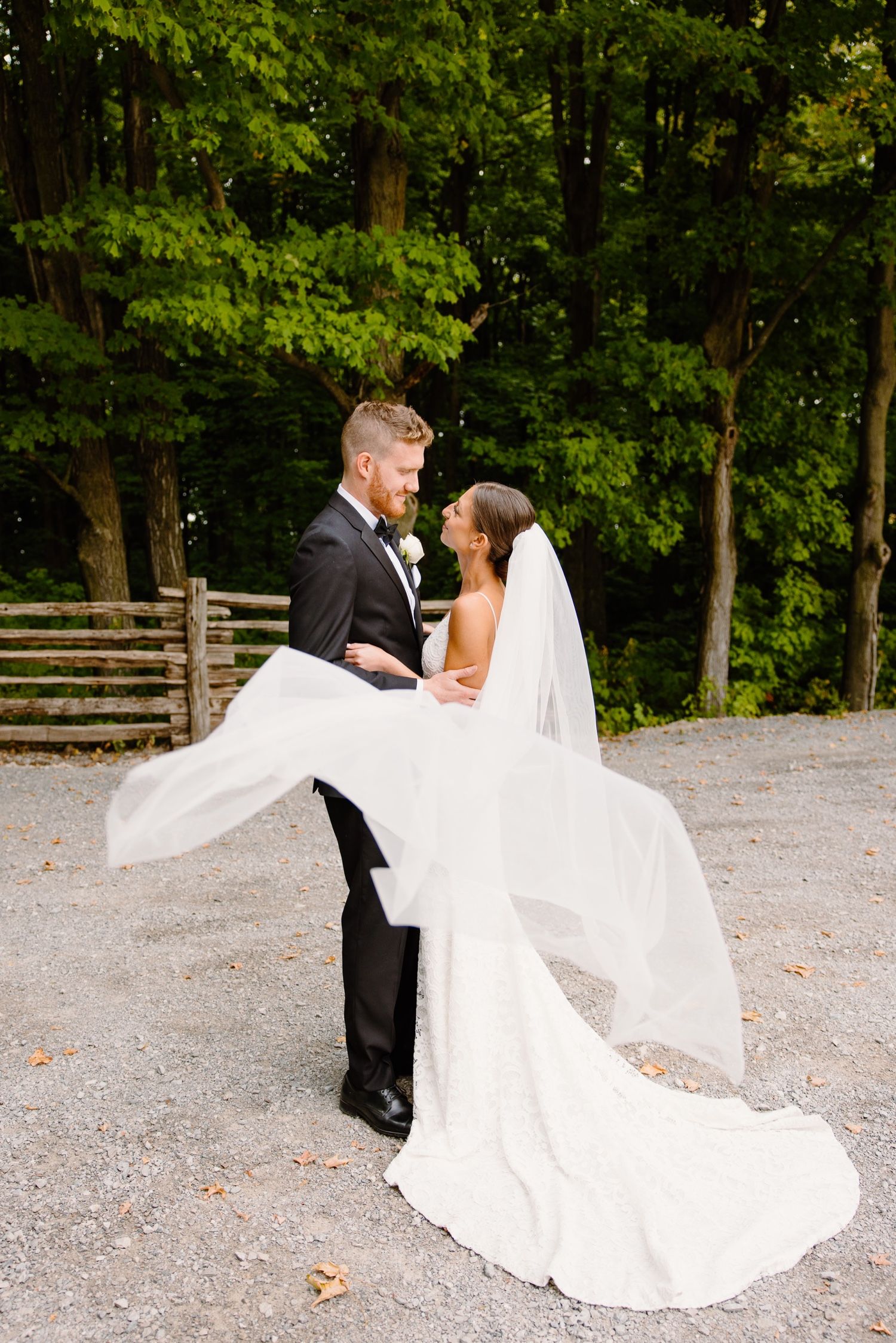 A romantic wedding photo shows a flowing white dress and veil lifted by the breeze against a wooded backdrop.
