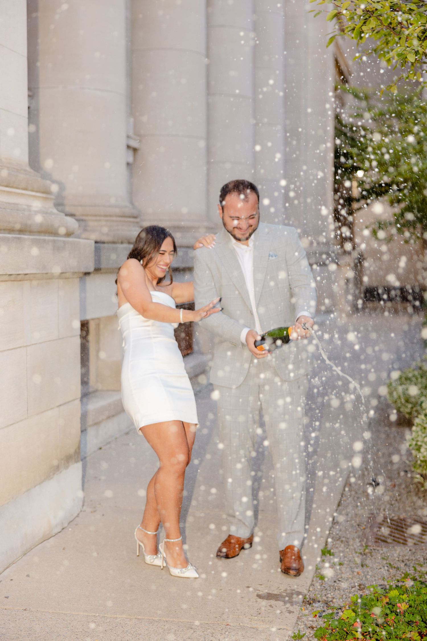 Joyful champagne celebration with spray against architectural backdrop.