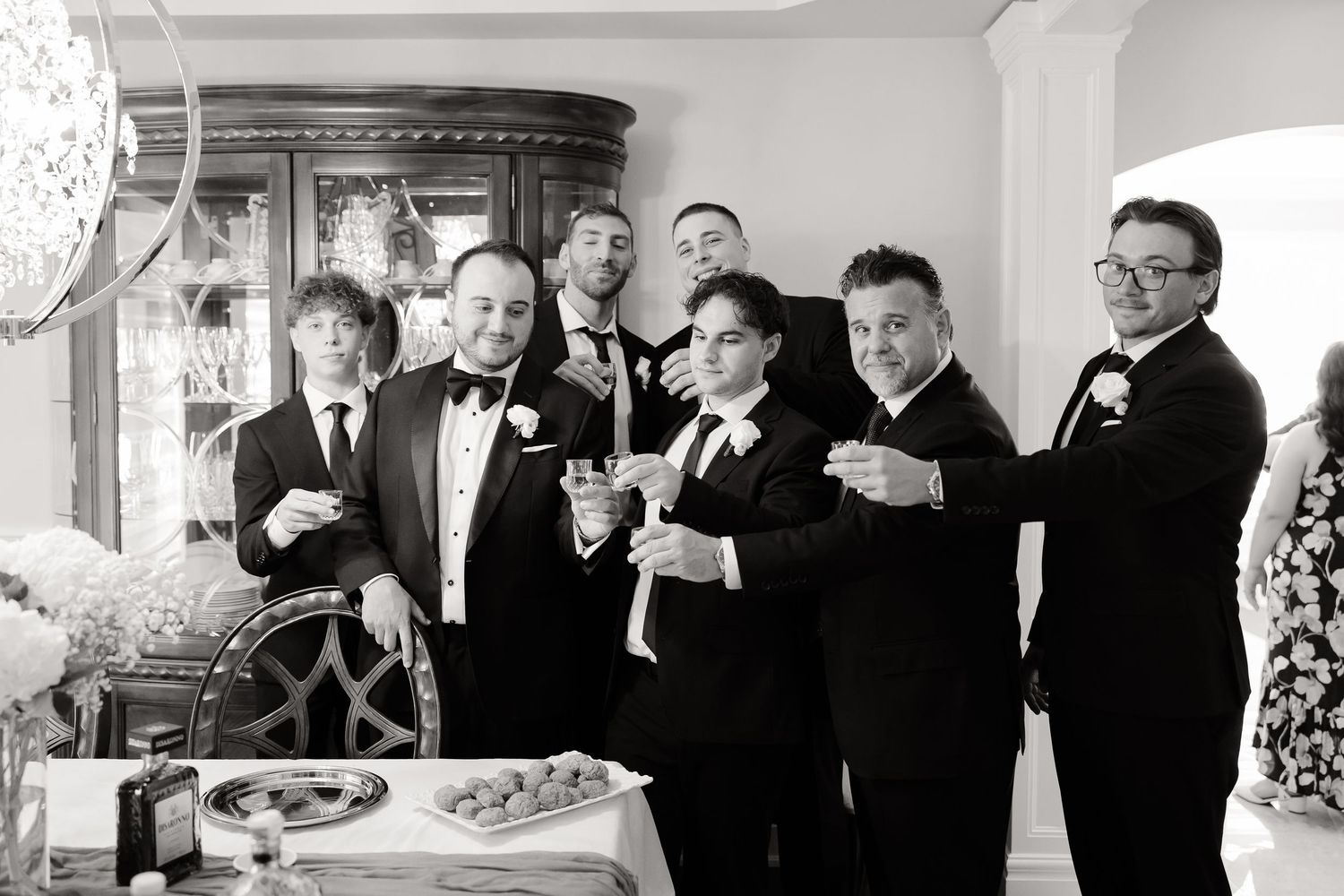 A vintage black and white photo showing a group in formal attire gathering around a table at a celebration.