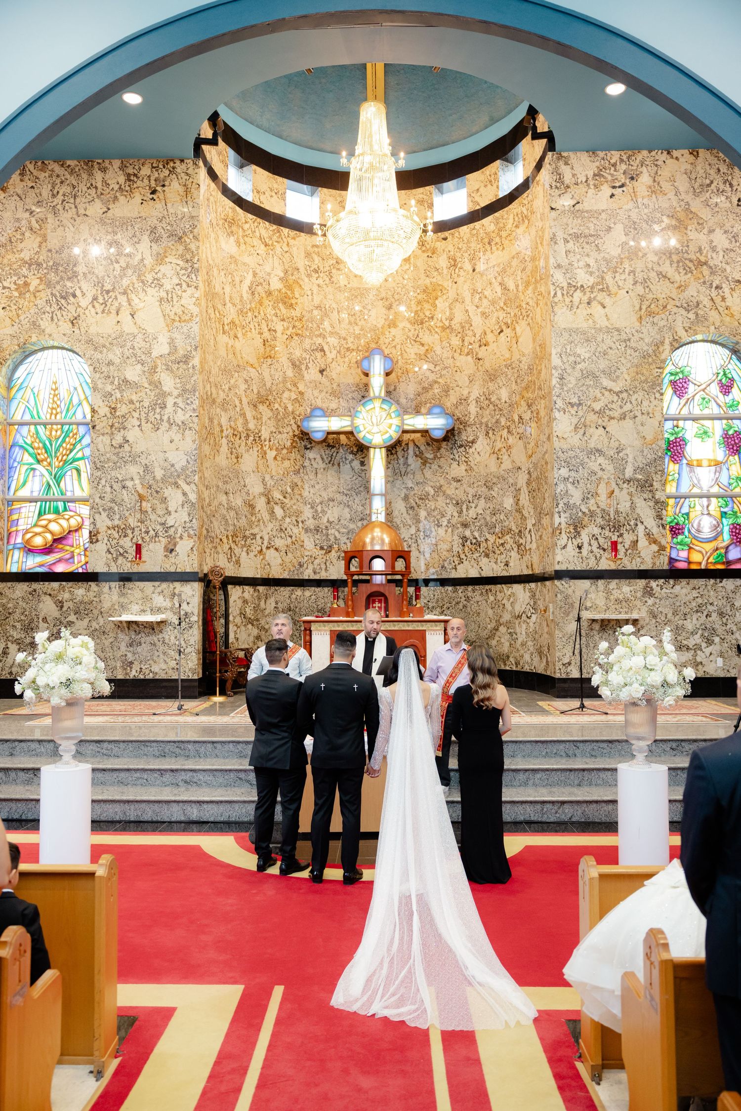 A wedding ceremony at a church altar with ornate chandelier and stained glass windows.