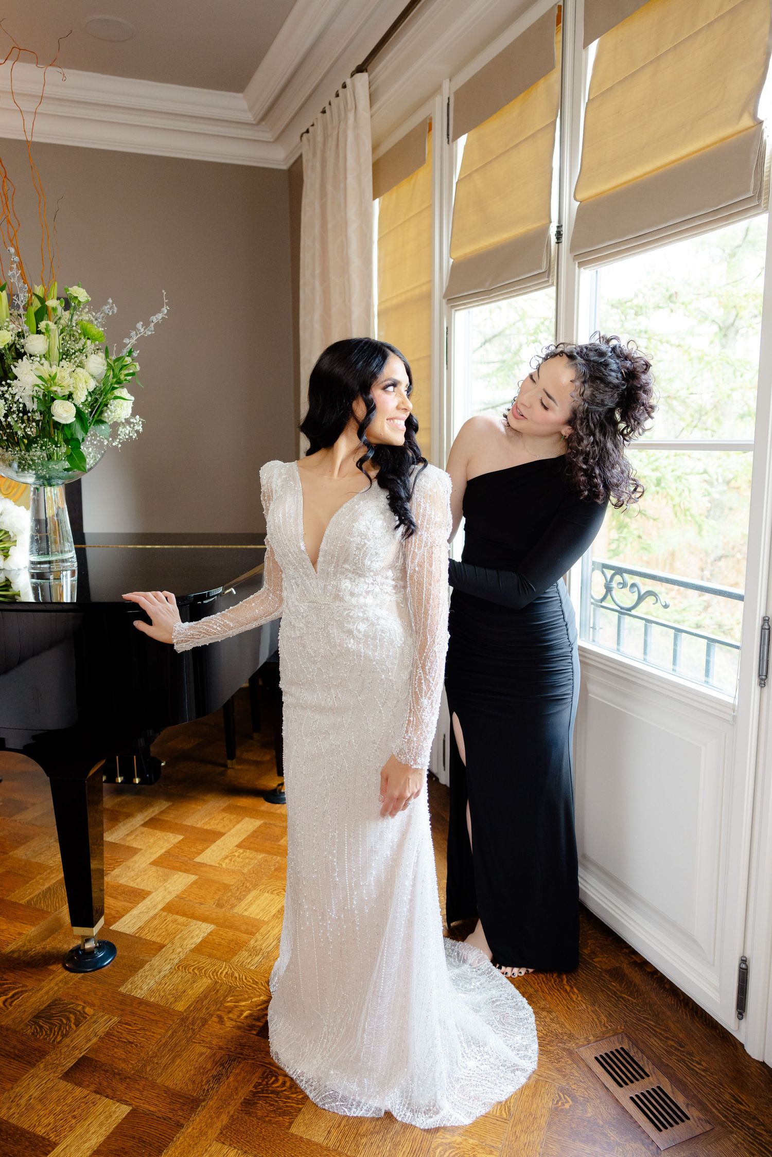 Elegant wedding dress fitting session in room with piano and floral arrangement.