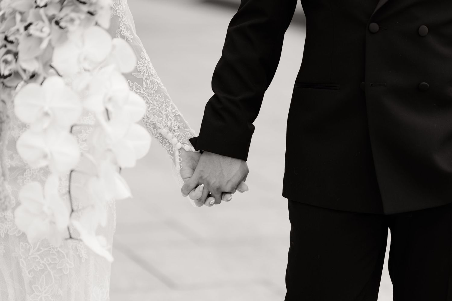 A black and white wedding photograph showing a couple holding hands while wearing formal wedding attire.