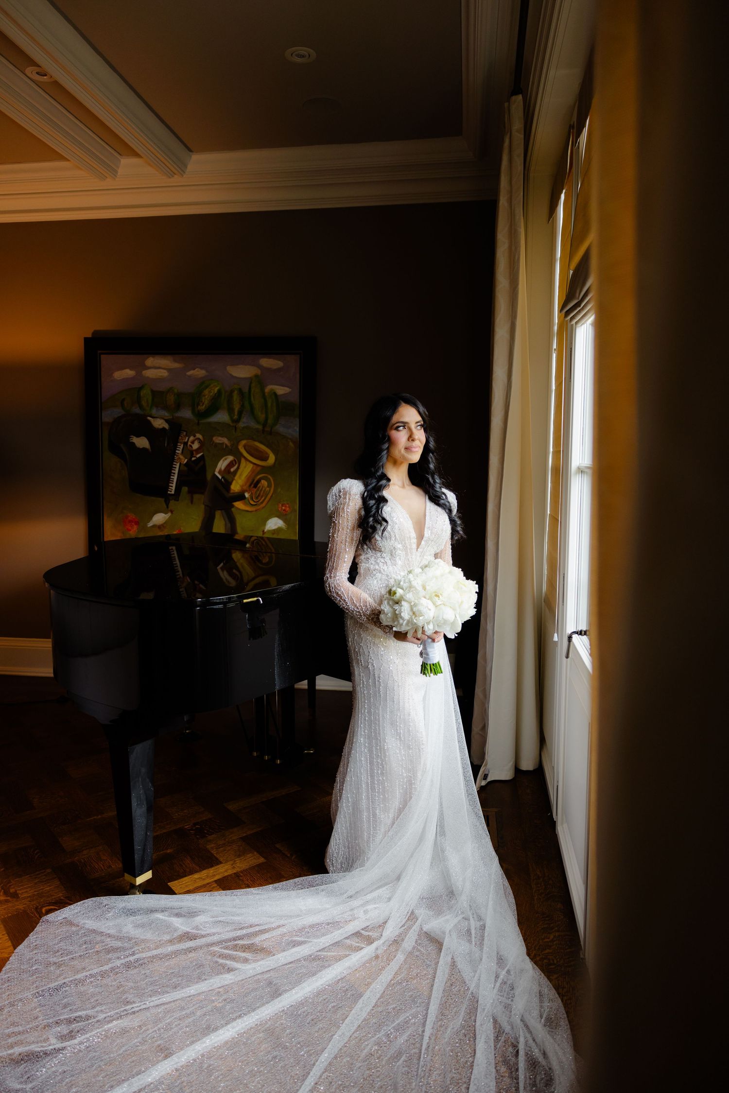 Bride in long-sleeve lace gown with cathedral train poses by window near grand piano.