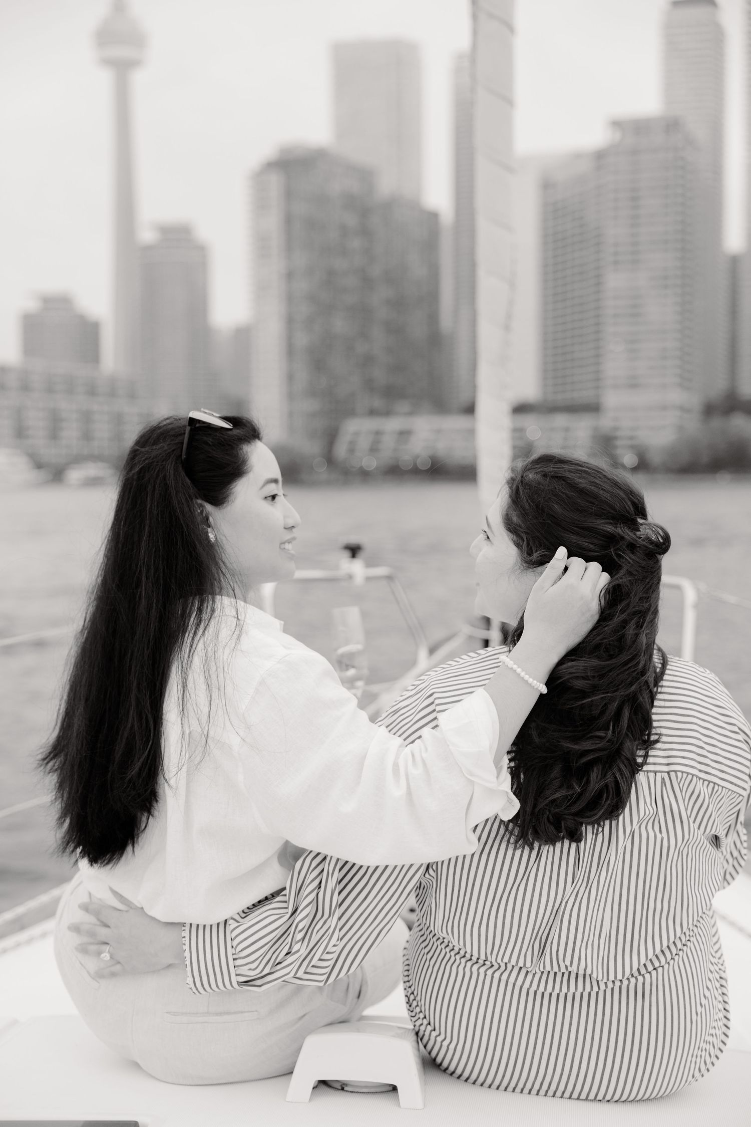 Two people in relaxed clothing sitting together with Toronto's iconic CN Tower skyline visible in black and white background.