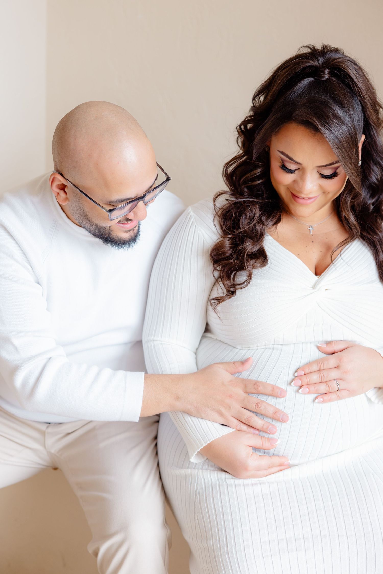 A couple in matching white outfits share an intimate moment during their maternity photoshoot.