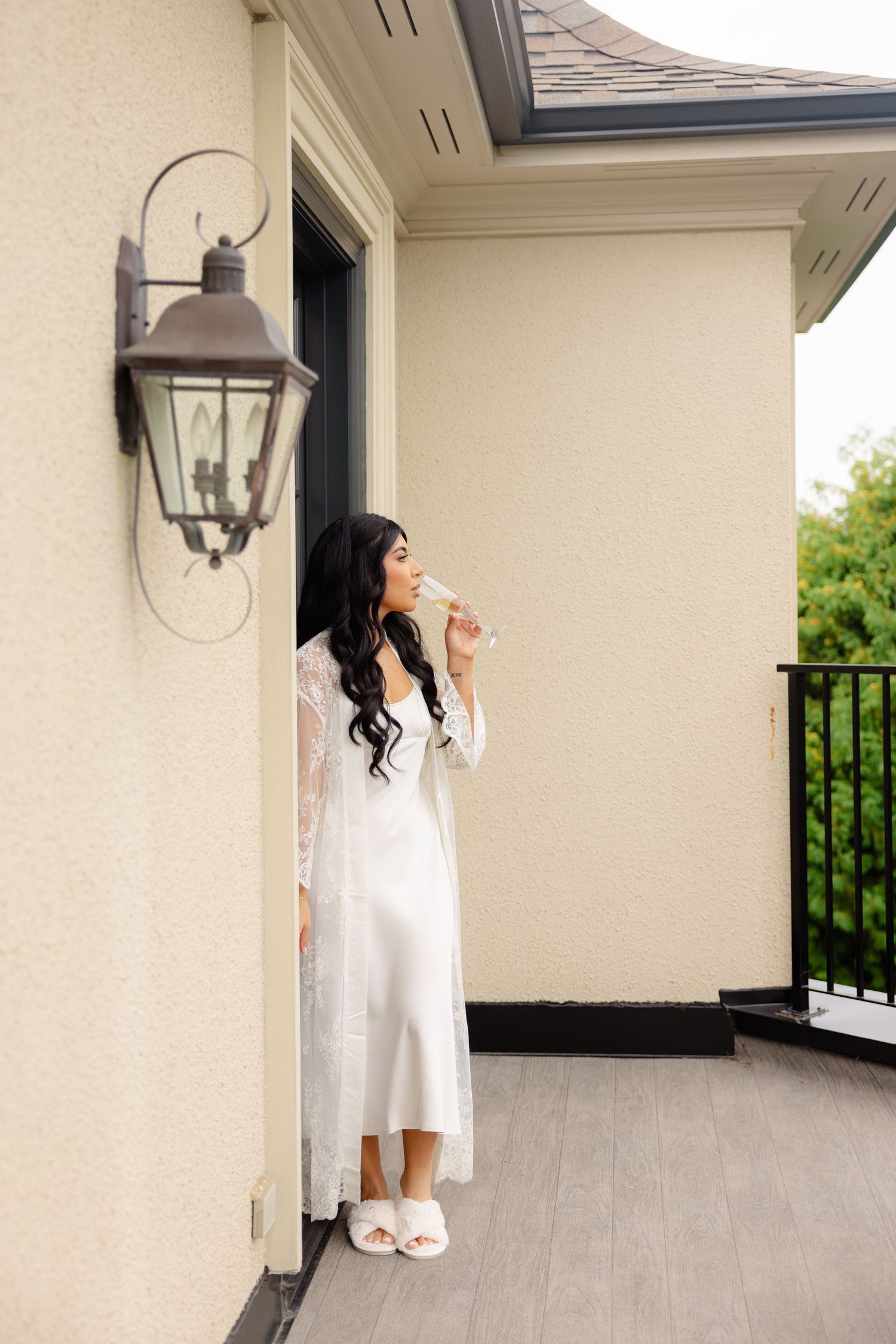 A woman in a white mini dress poses gracefully on a covered outdoor patio with stone columns and railings.