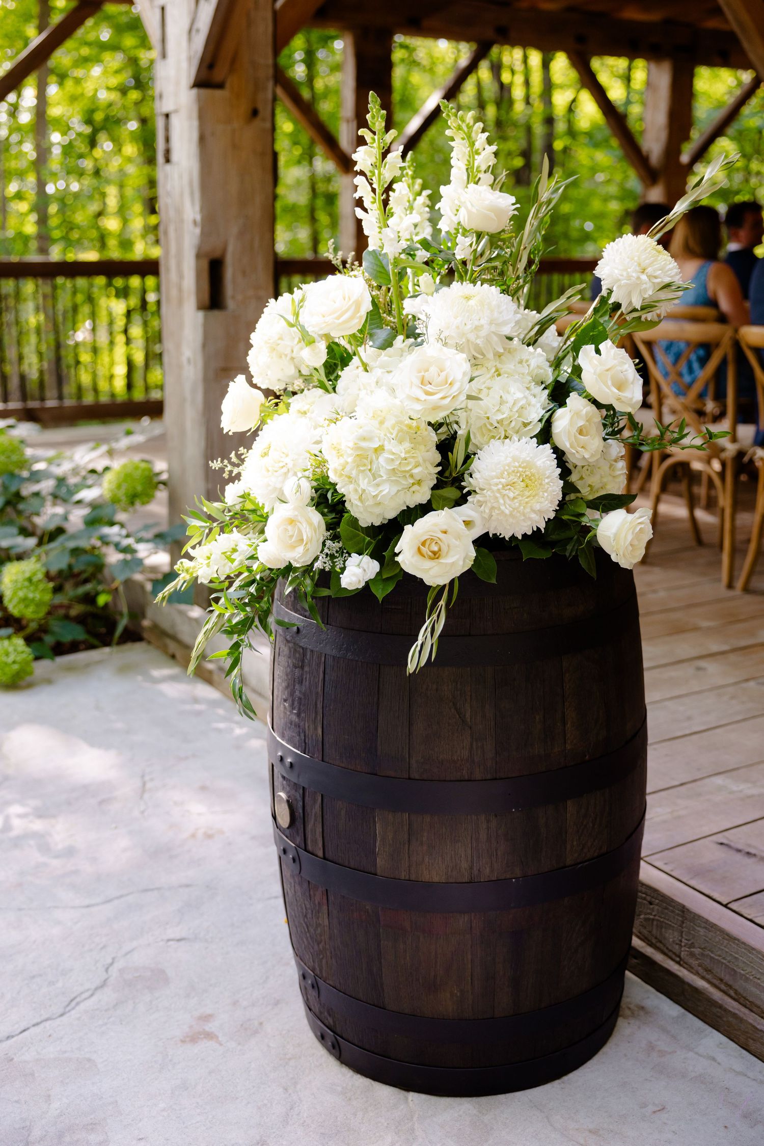 White floral arrangement in a rustic wooden barrel on a covered outdoor patio.