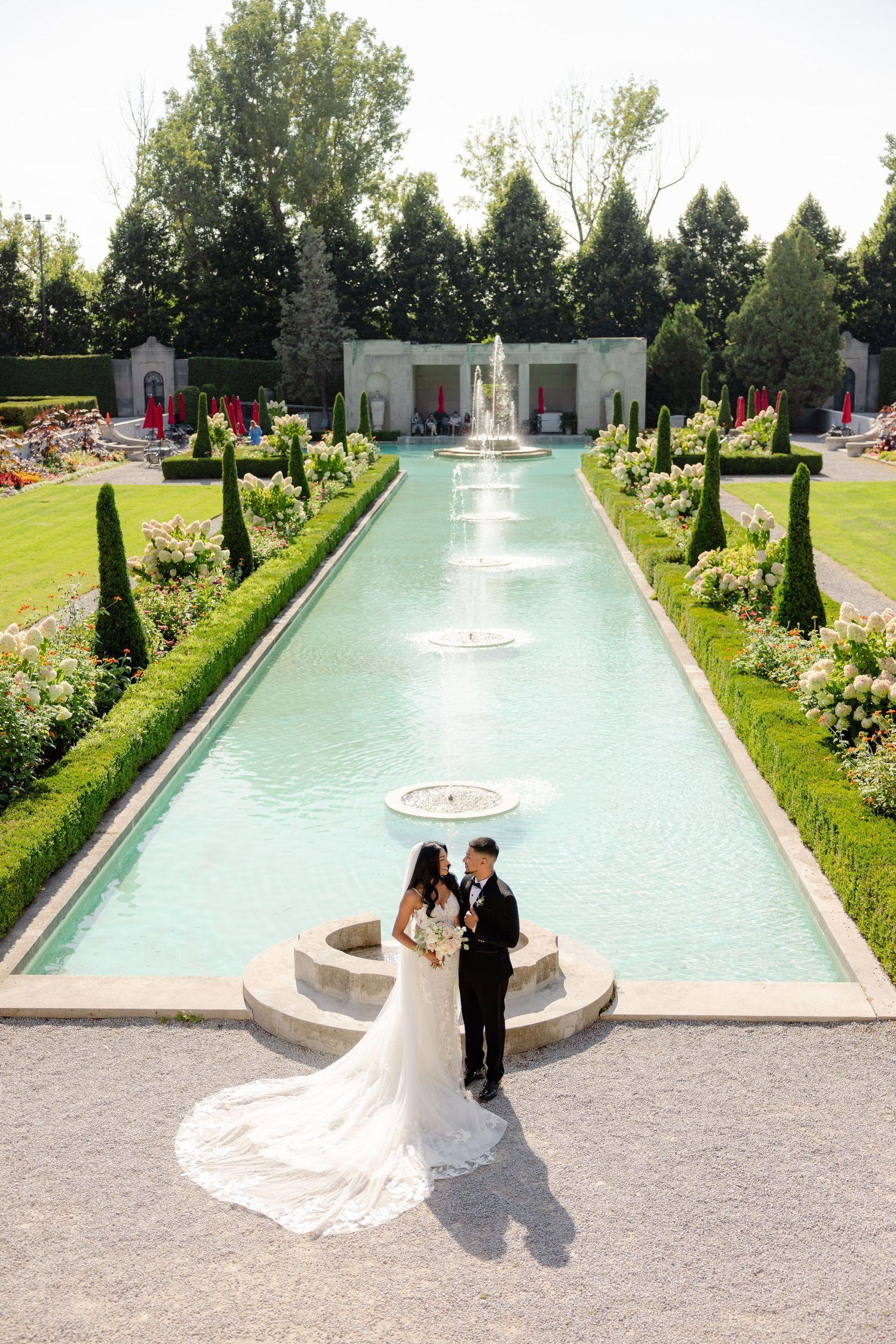 Romantic wedding photo beside an ornate reflecting pool in a perfectly manicured formal garden.