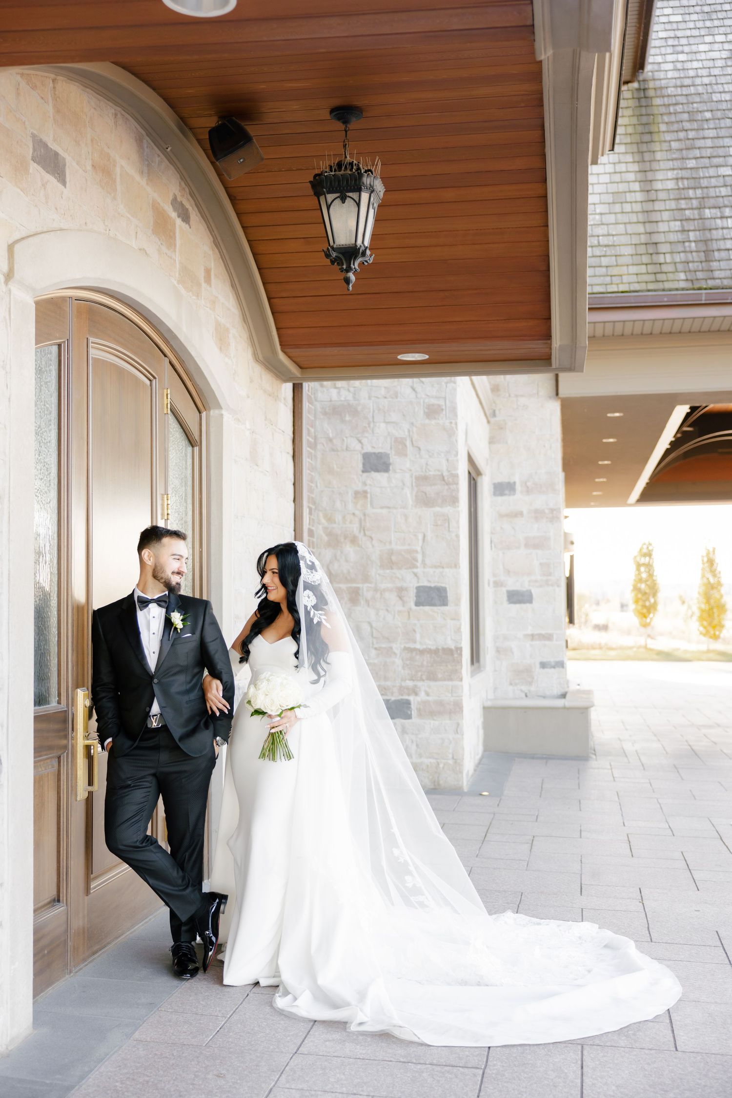 Elegant wedding couple poses in entryway with stone walls and wooden ceiling details.