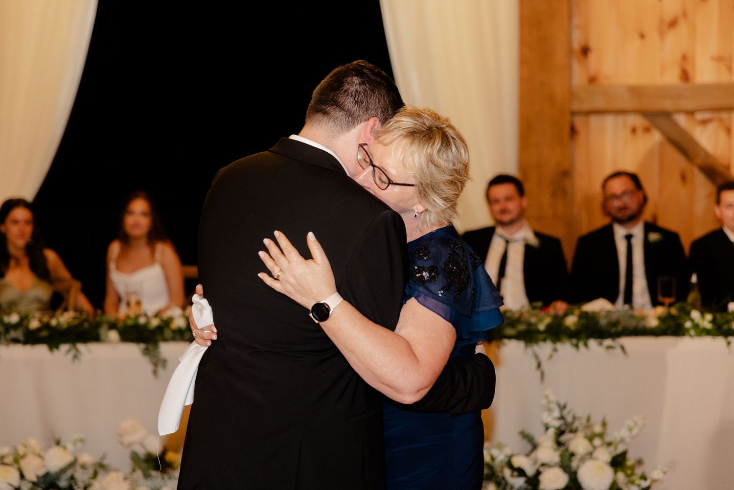 Two people share a tender embrace during a wedding dance in a rustic barn venue.