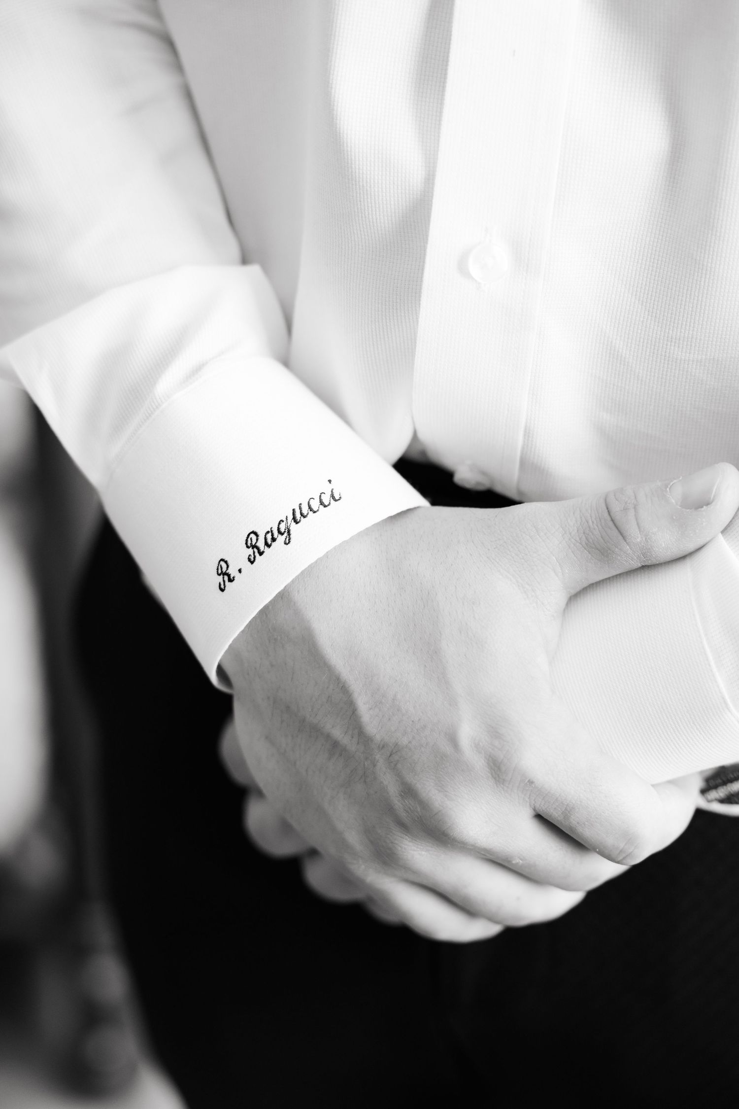 Close-up of monogrammed white shirt cuff with elegant cursive text embroidered on the fabric.