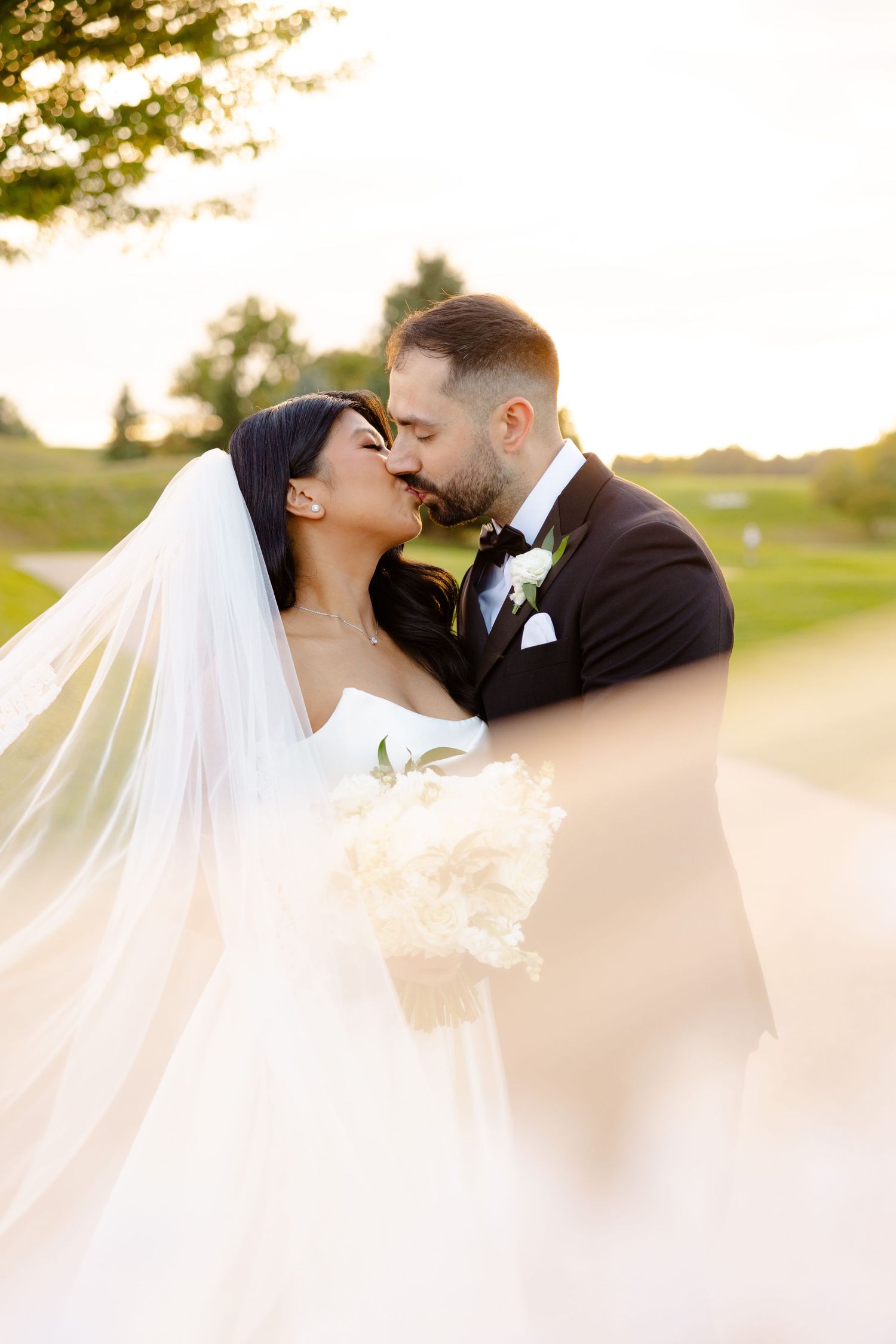 A romantic moment between newlyweds at sunset on a golf course with a flowing veil.