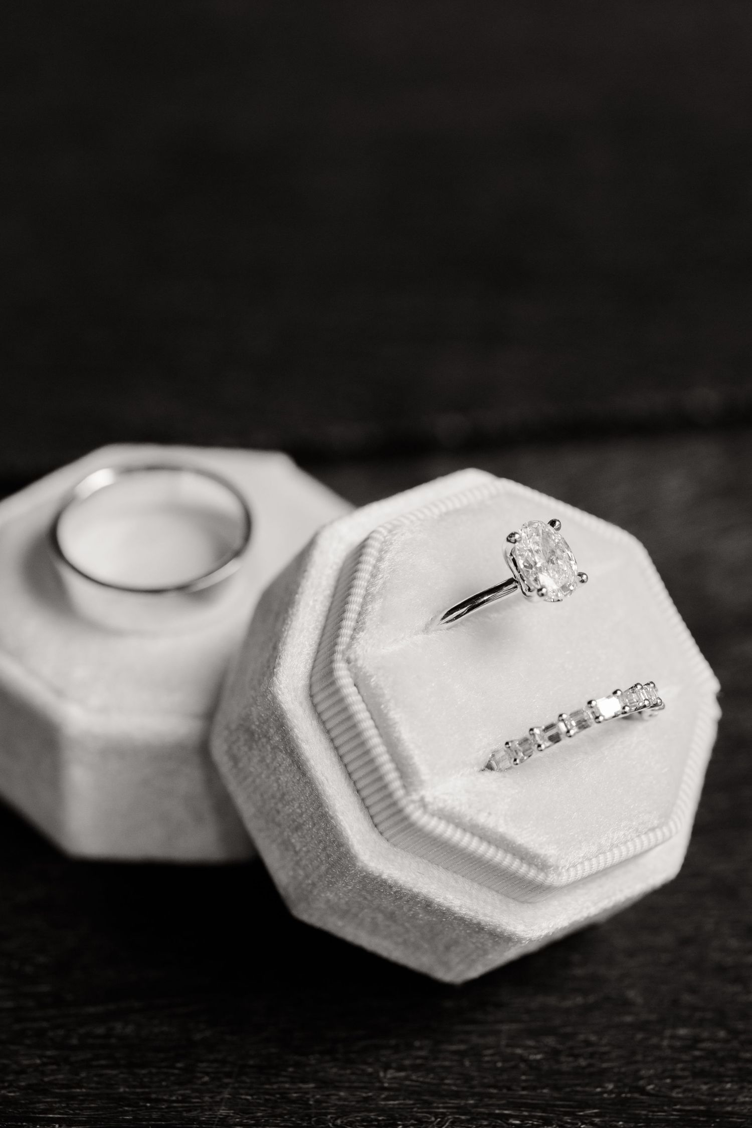Black and white photo of wedding rings nestled in white octagonal ring boxes.