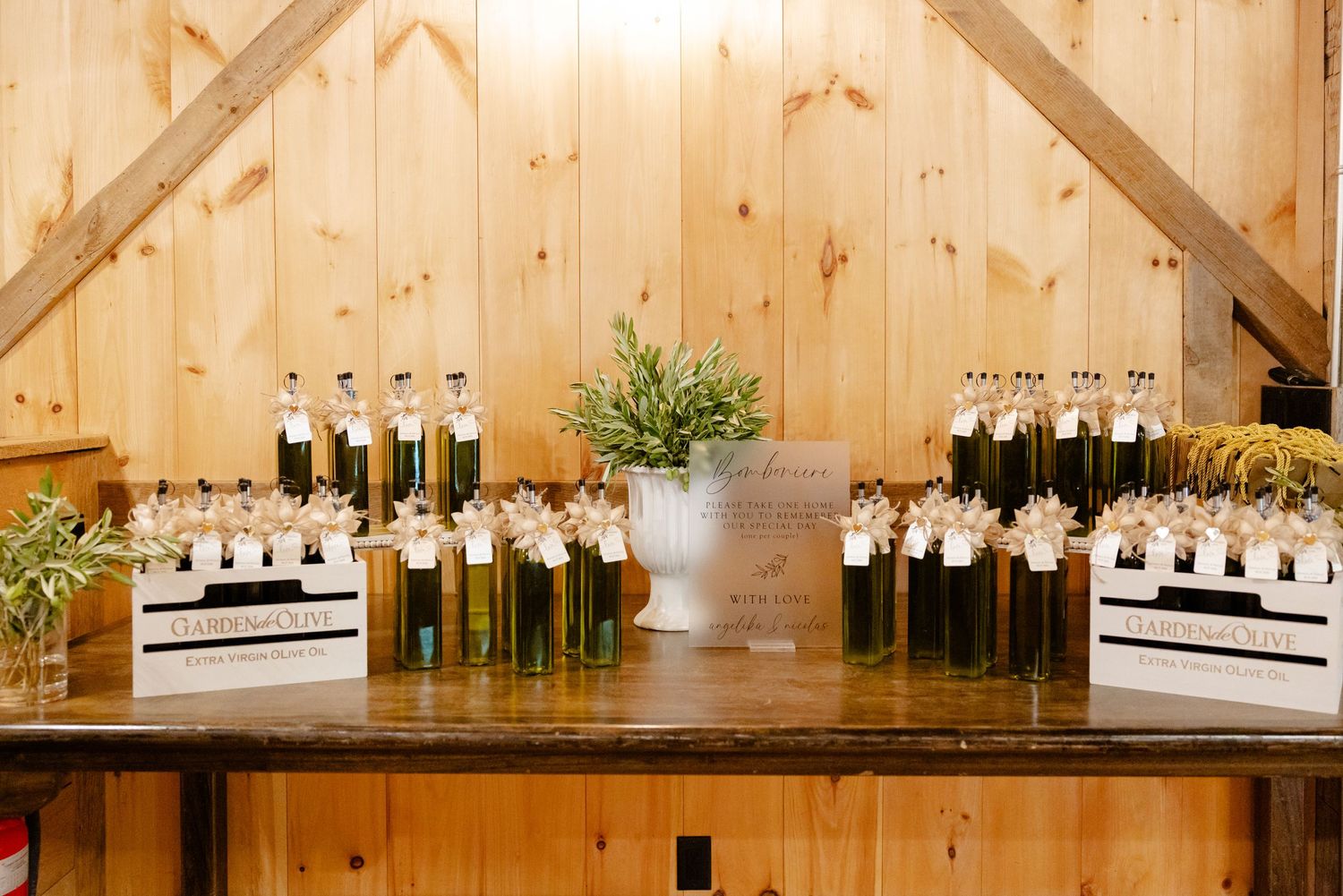 Elegant olive oil bottle wedding favors displayed in rustic wooden crates against pine walls.