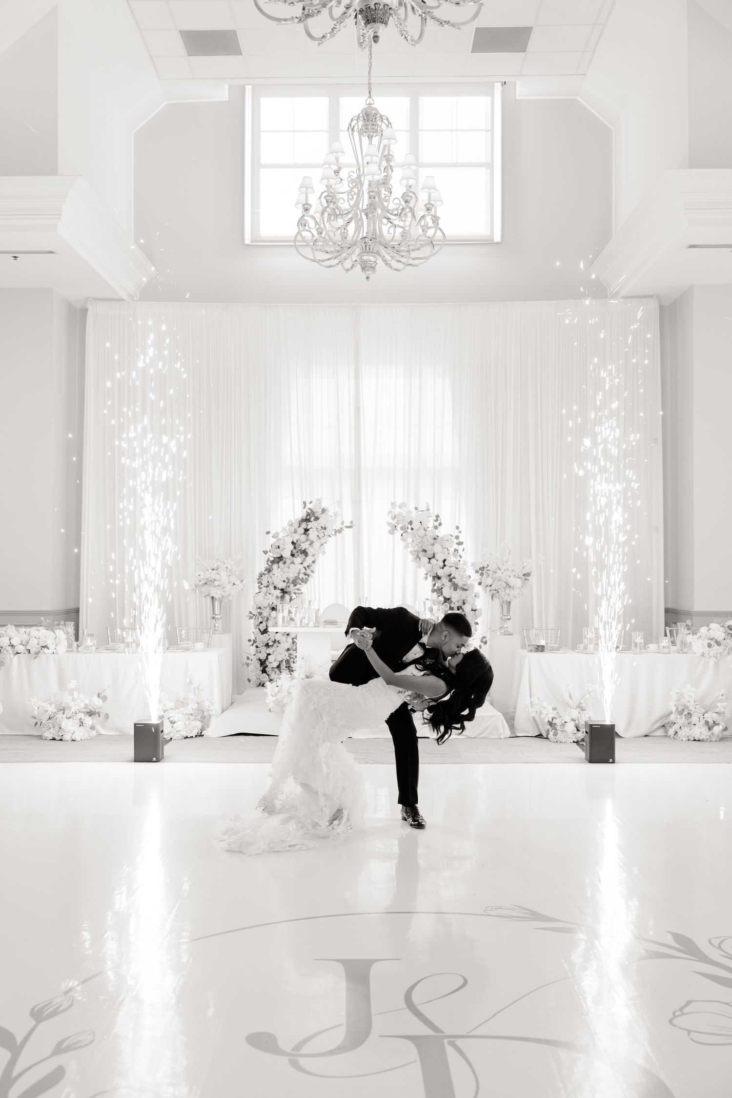 Black and white photo of wedding dance dip in elegant ballroom with monogrammed floor.