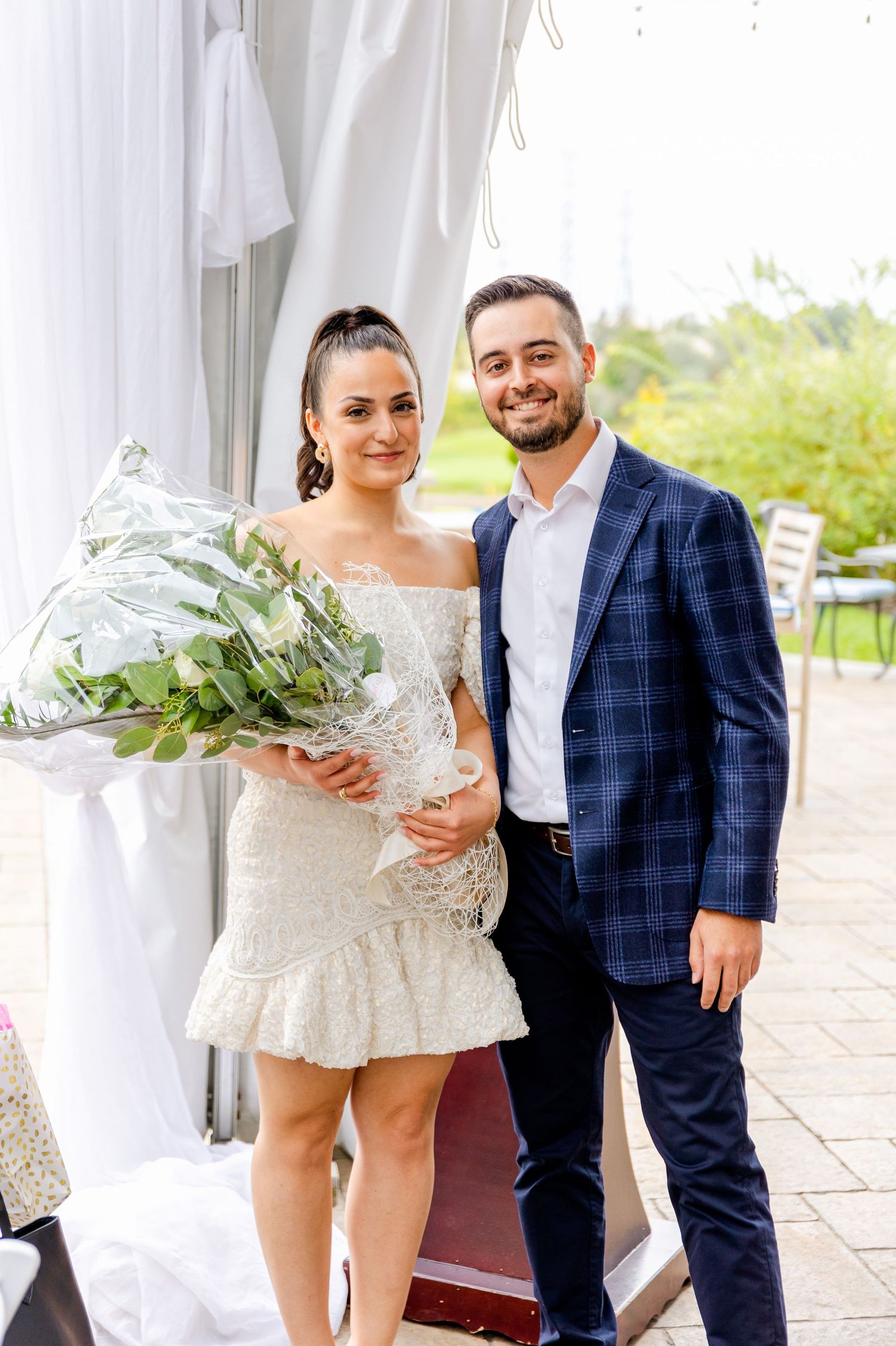 Couple poses with floral bouquet at elegant outdoor event.