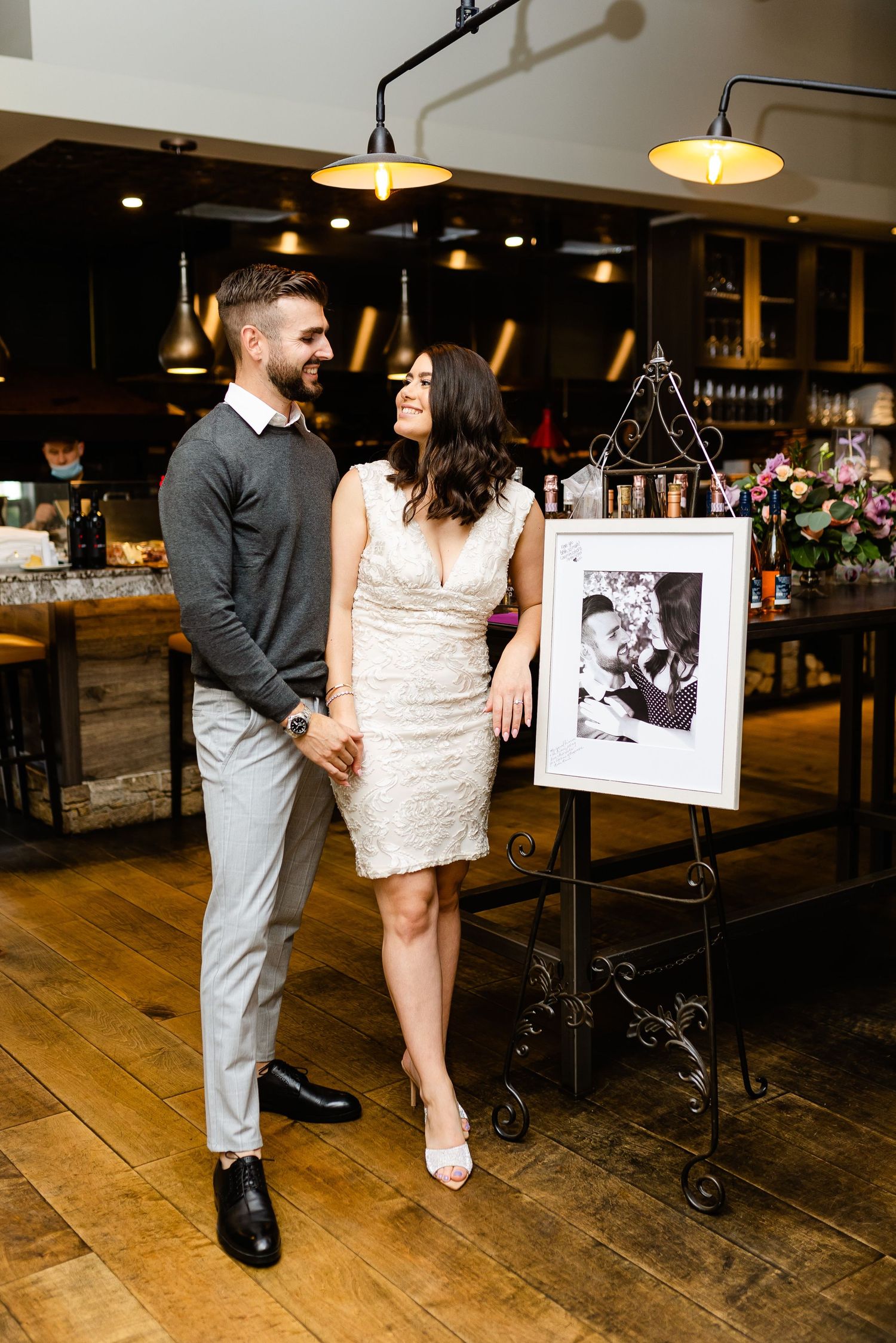 Stylishly dressed couple posing in restaurant with framed photo display and wooden floors.