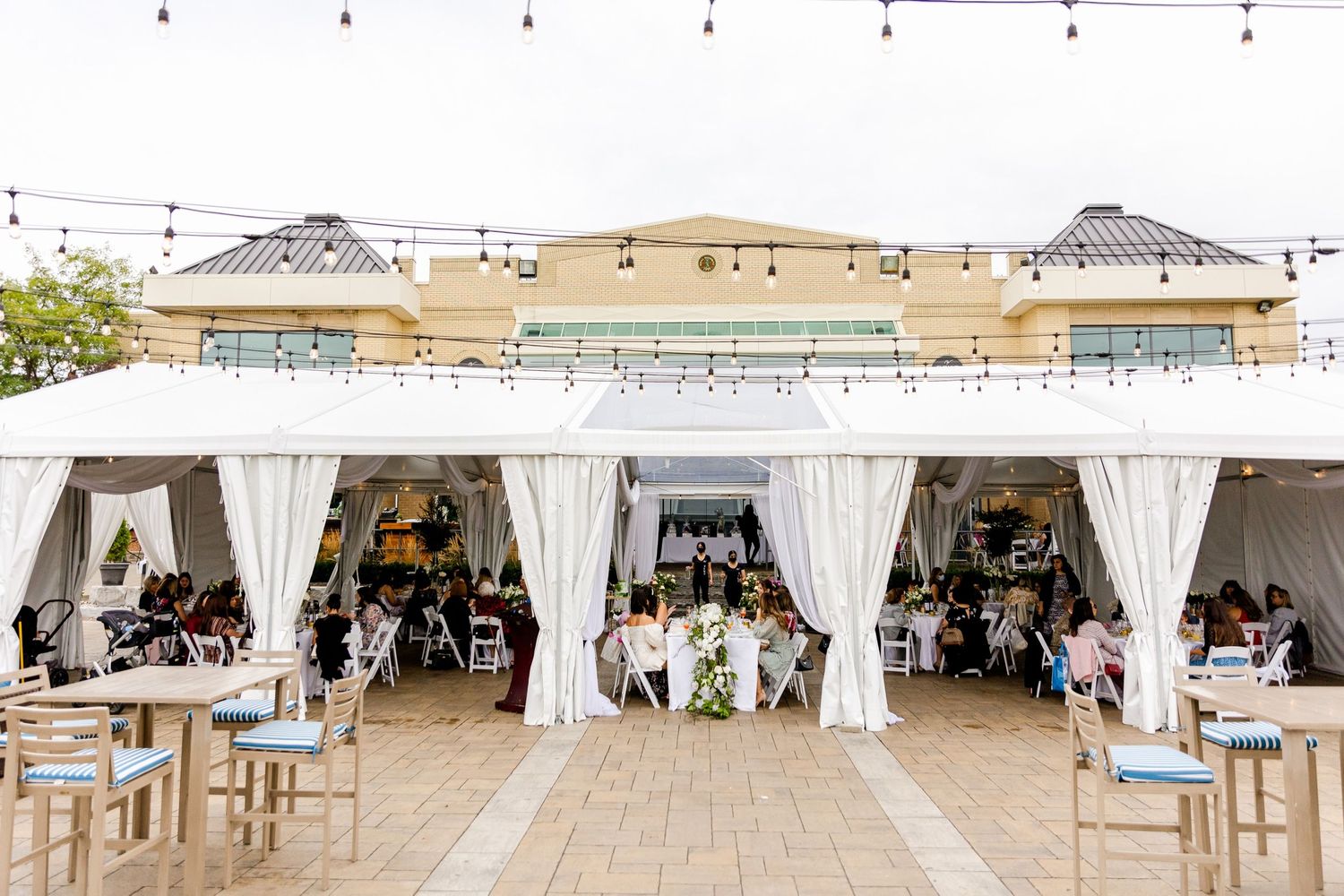 Outdoor wedding venue with white draped cabanas and dining tables set up on a patio.