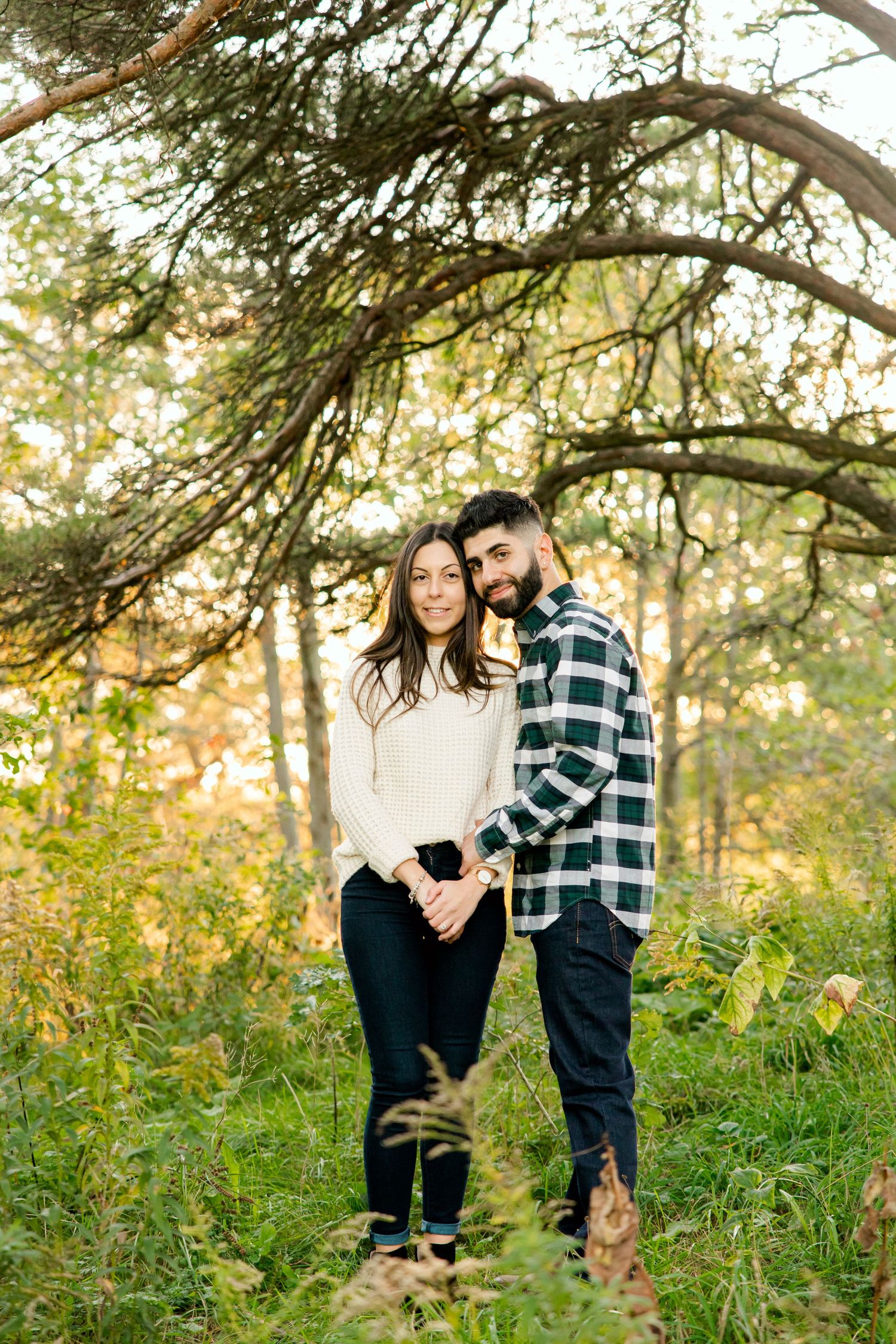 A couple shares a romantic moment under tree branches in an outdoor autumn setting.