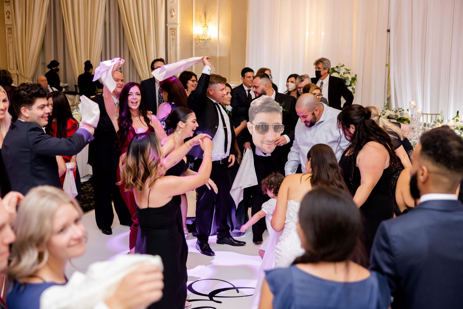 Energetic wedding guests dancing and celebrating with napkins in the air at a reception.