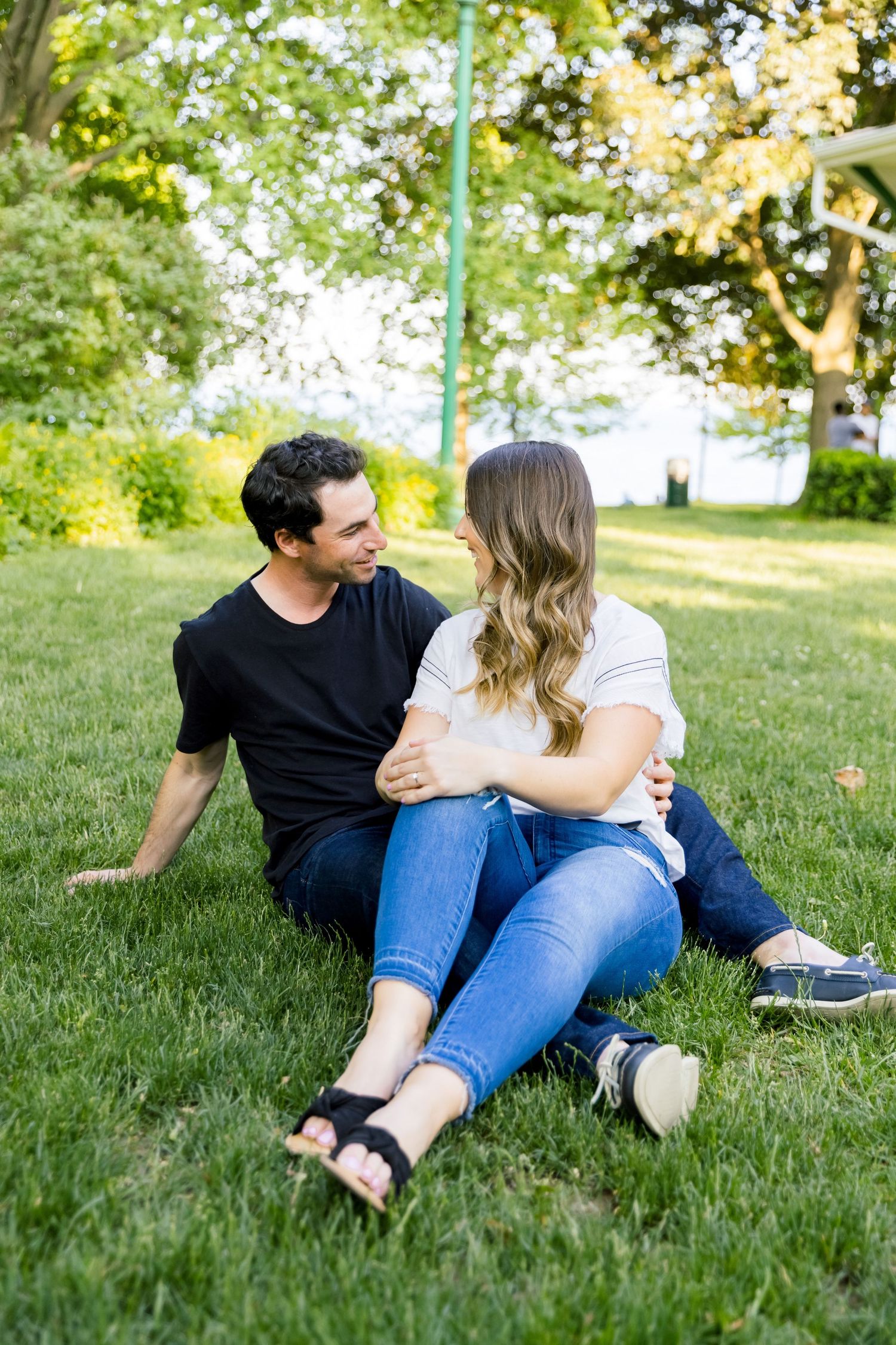 A couple relaxes together on a sunny lawn surrounded by trees.