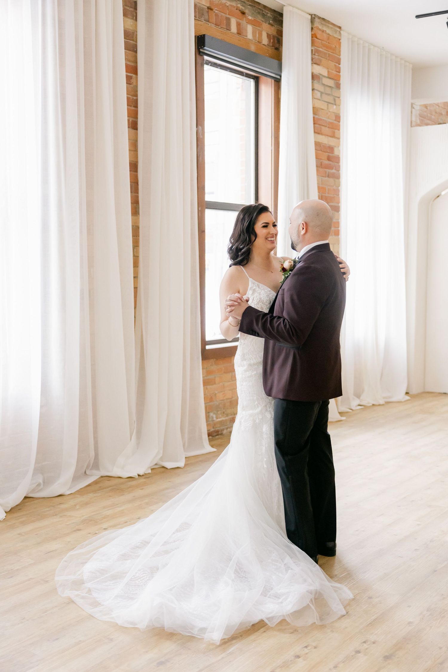 A romantic moment in a sunlit room with exposed brick walls and flowing white curtains.