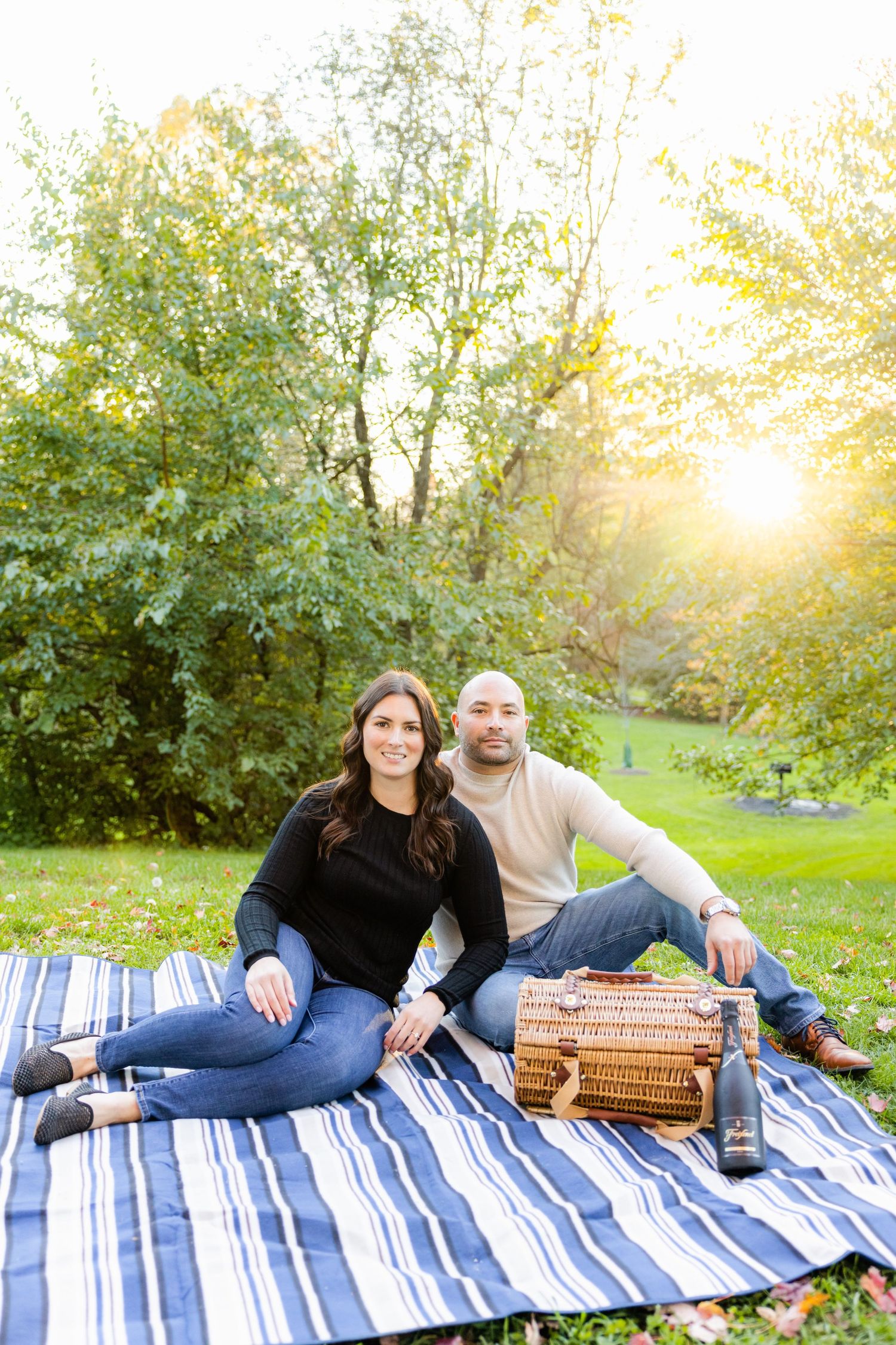 Romantic outdoor picnic scene with couple relaxing on blue striped blanket at sunset.