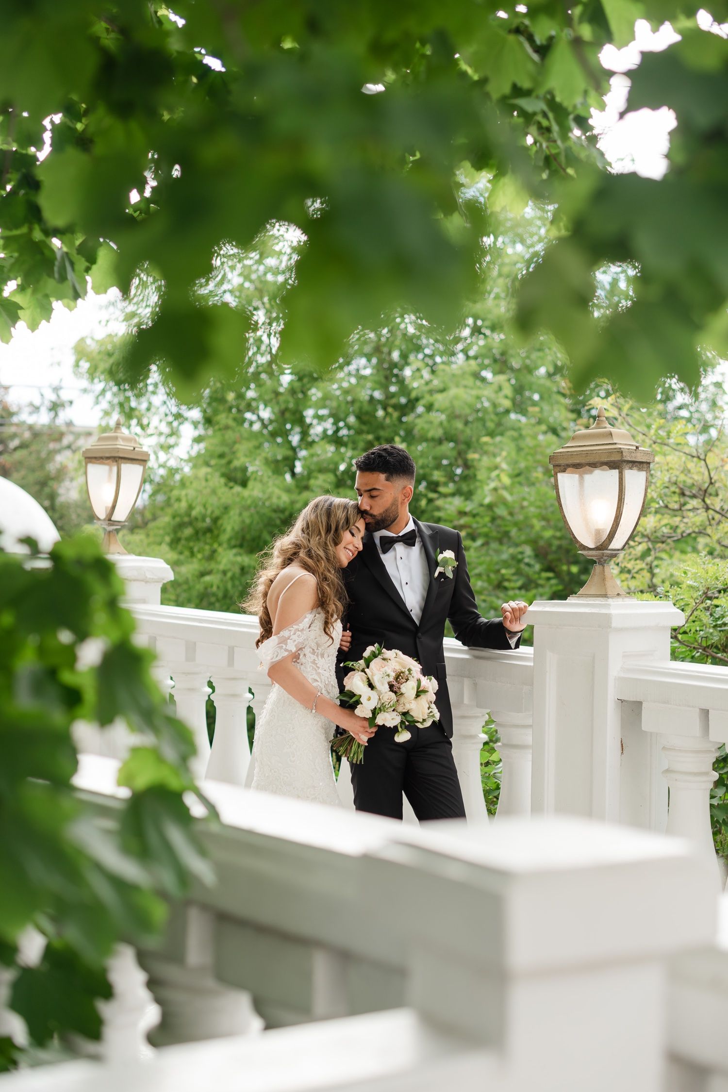 Romantic moment captured between newlyweds on white balustrade with glowing lanterns.