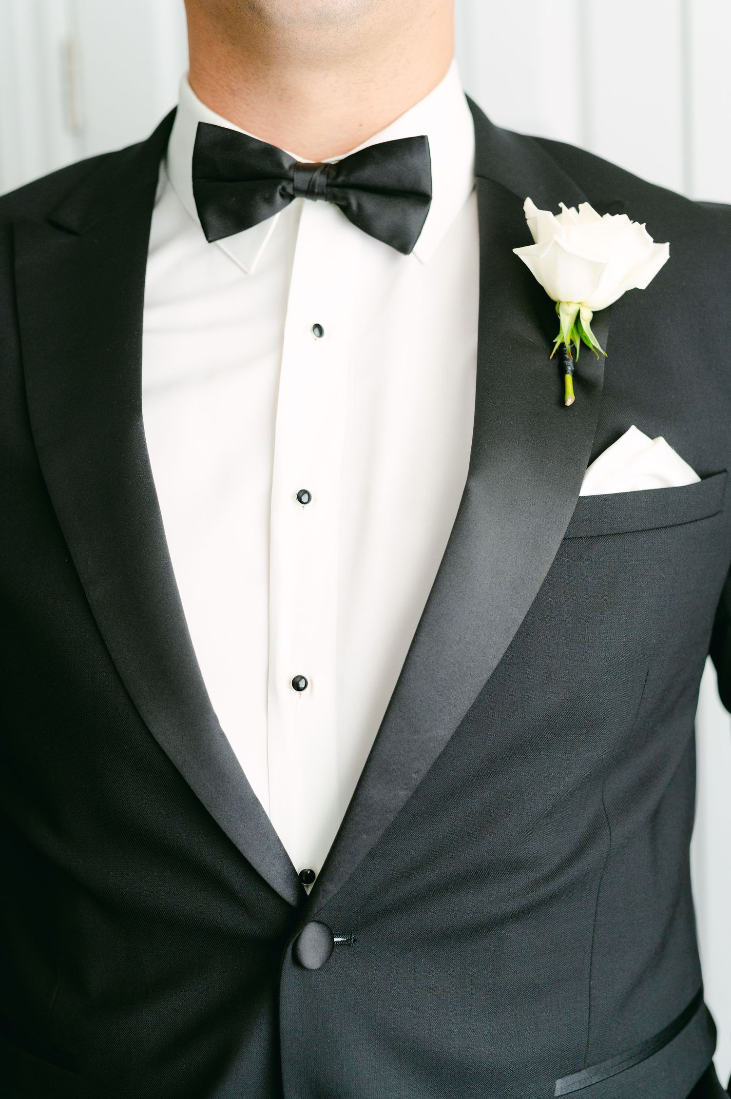 Detail shot of a classic tuxedo with black bow tie and white rose boutonniere.