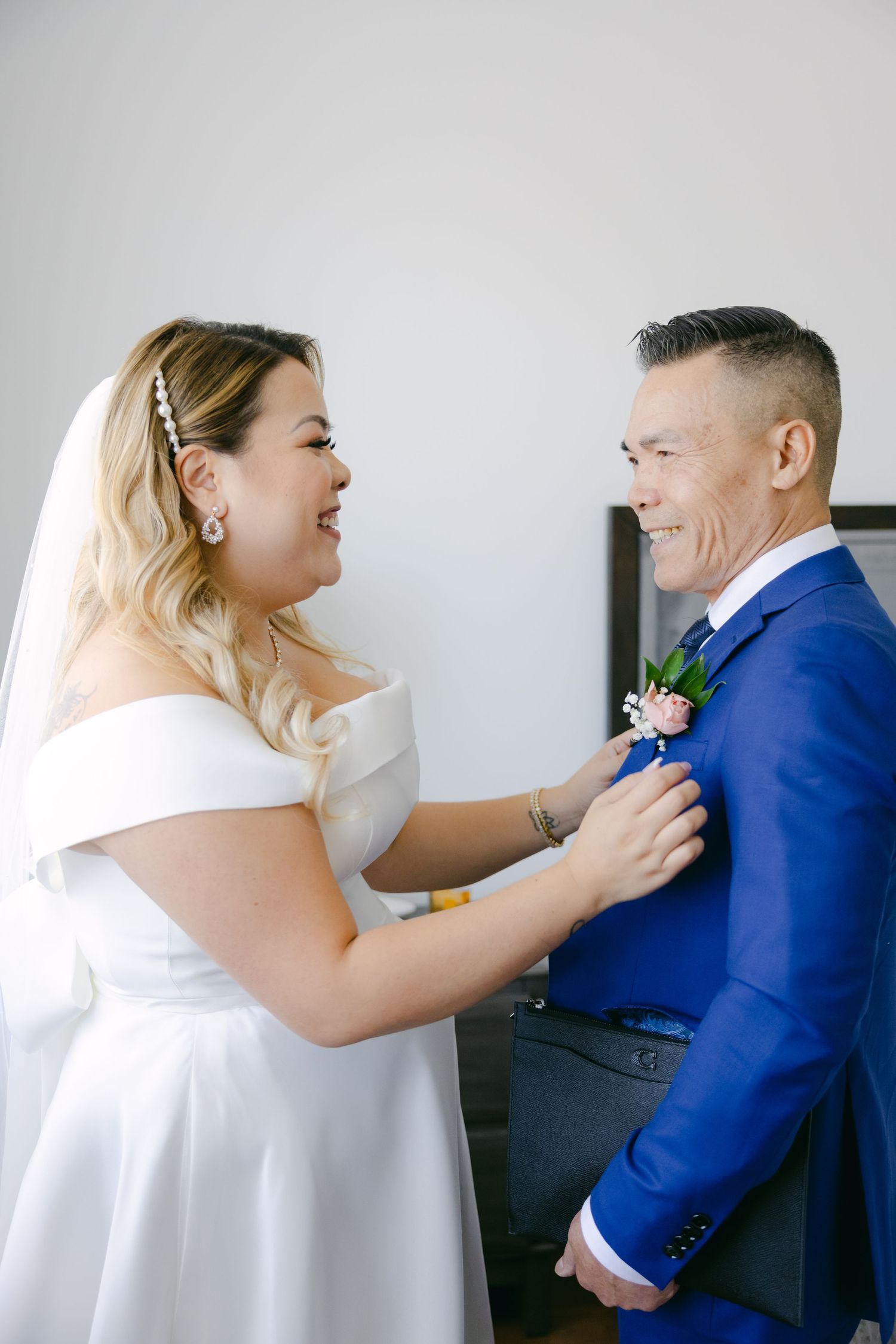 Bride pins boutonniere on groom's bright blue suit jacket during wedding preparations.