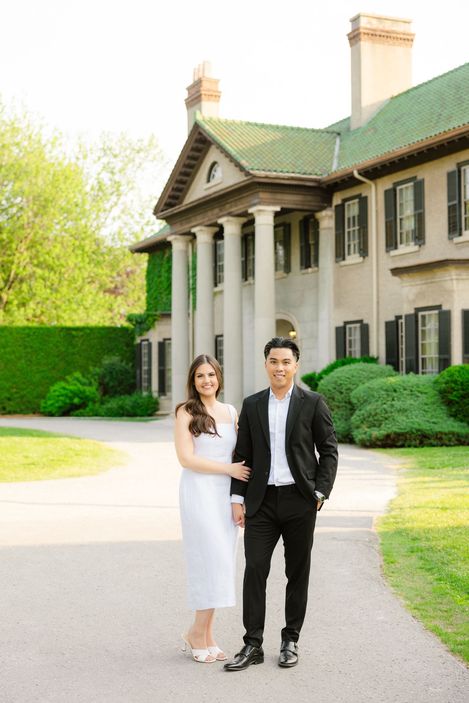 Formal portrait of couple standing in front of historic property with green roof and columns.