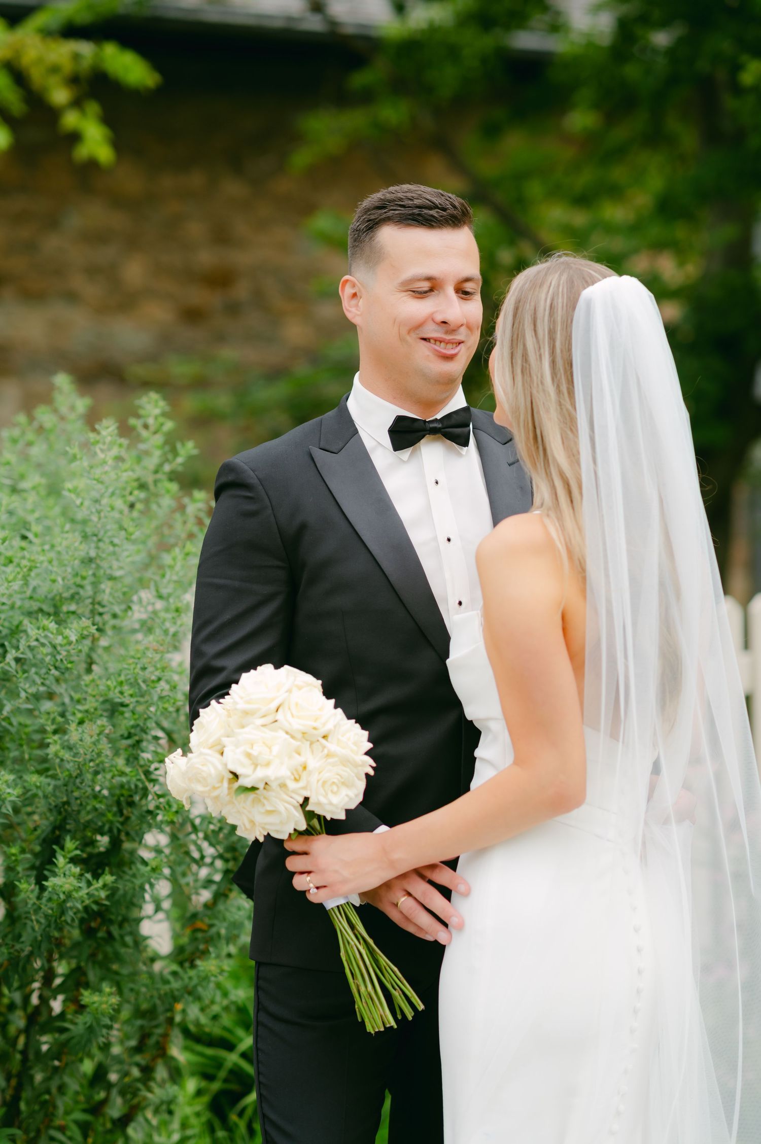 Elegant couple shares tender moment in garden with classic white rose bouquet.