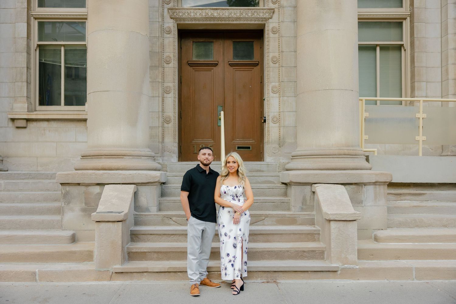 A couple poses on grand stone steps in front of a wooden door of a historic building.