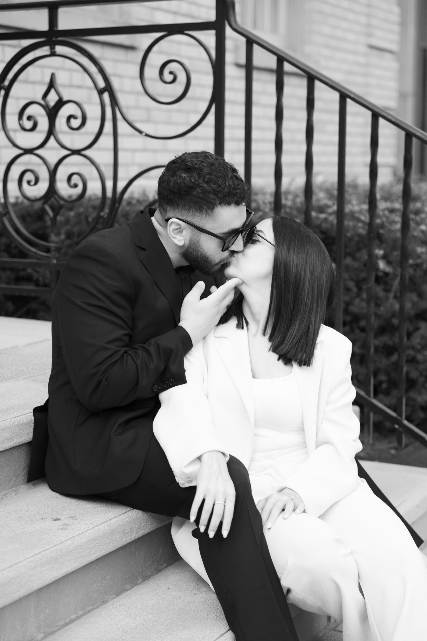 Close-up black and white photo showing an intimate moment on stone steps with decorative iron railing.