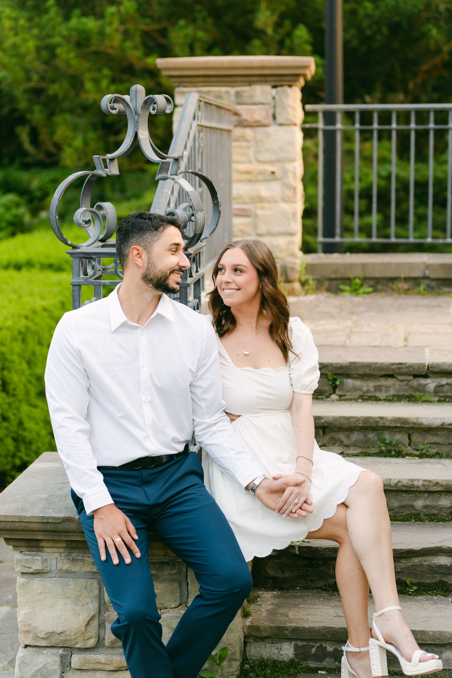 Couple shares an intimate moment while sitting on stone steps near ornate metal railing.