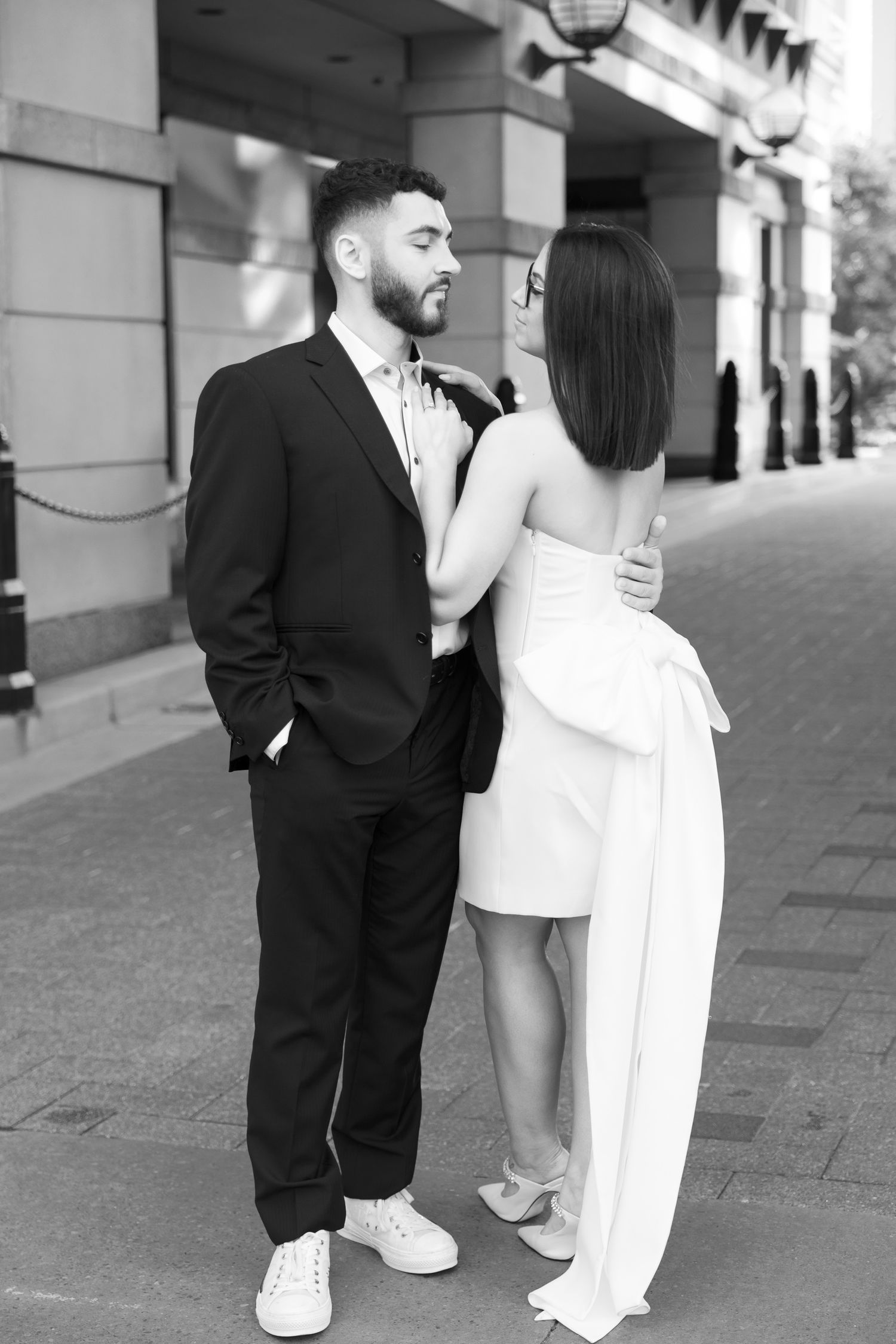 A romantic black and white portrait of a couple in formal wear standing close on a city street.