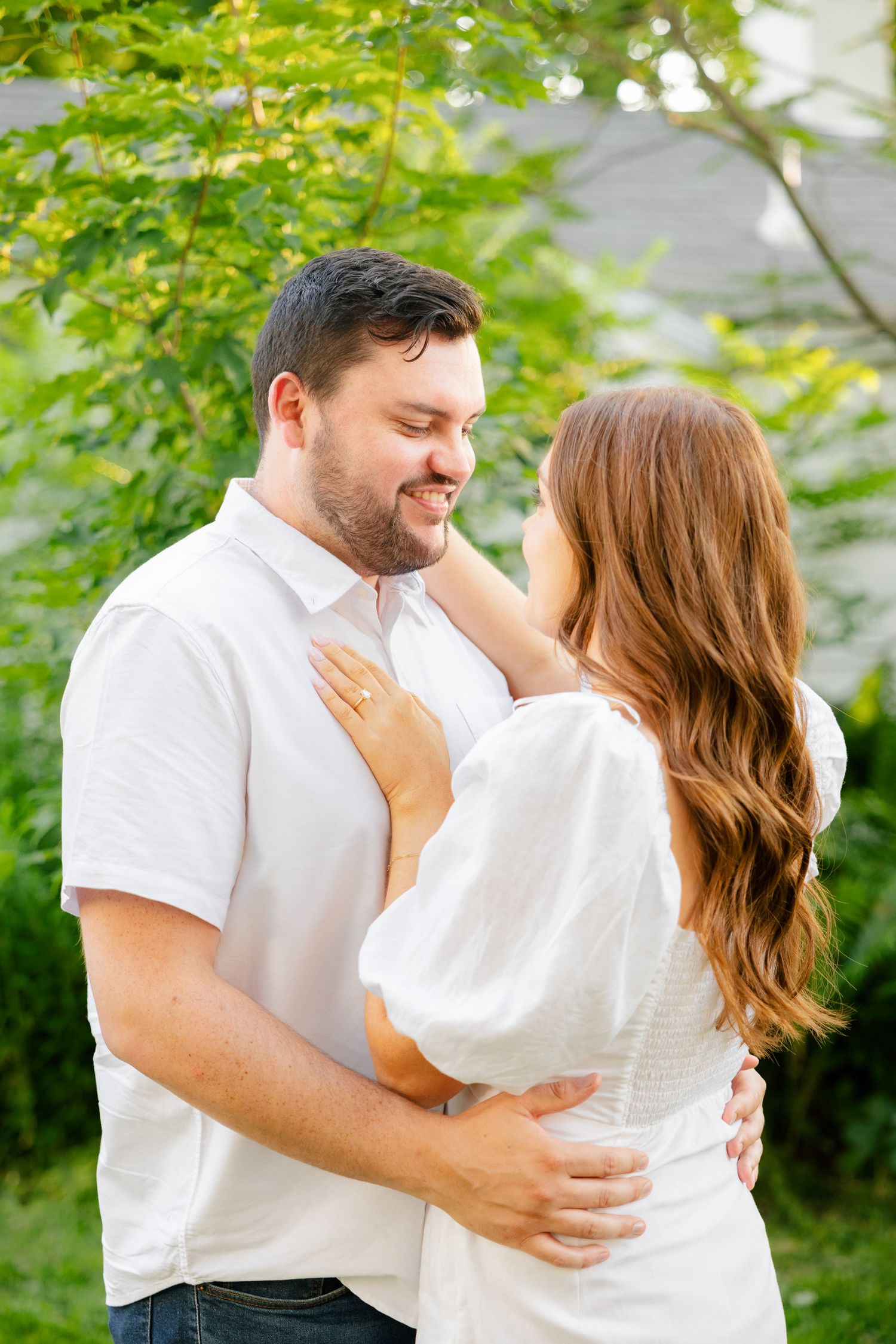A sweet outdoor couples portrait with both wearing white against a leafy green background.