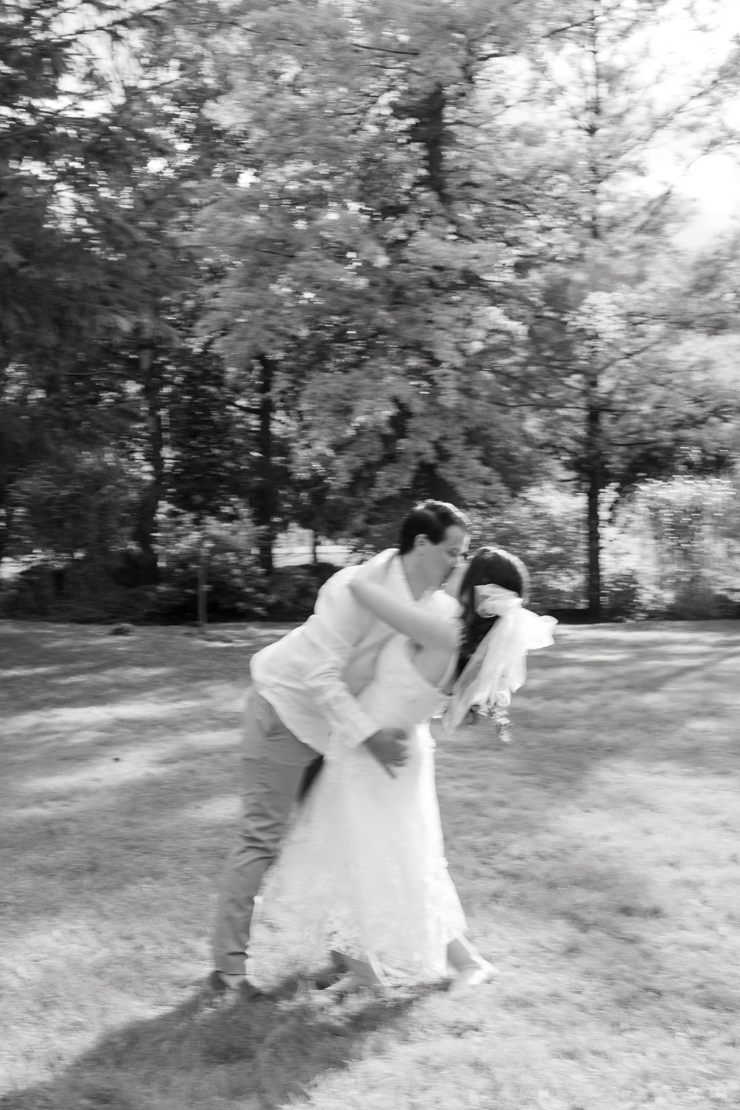 A romantic black and white photo of newlyweds sharing a dance move in a garden.
