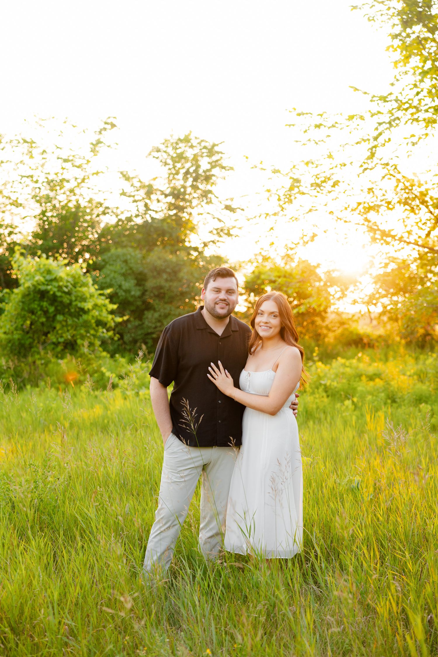 Happy couple poses together in summer field with warm evening light.