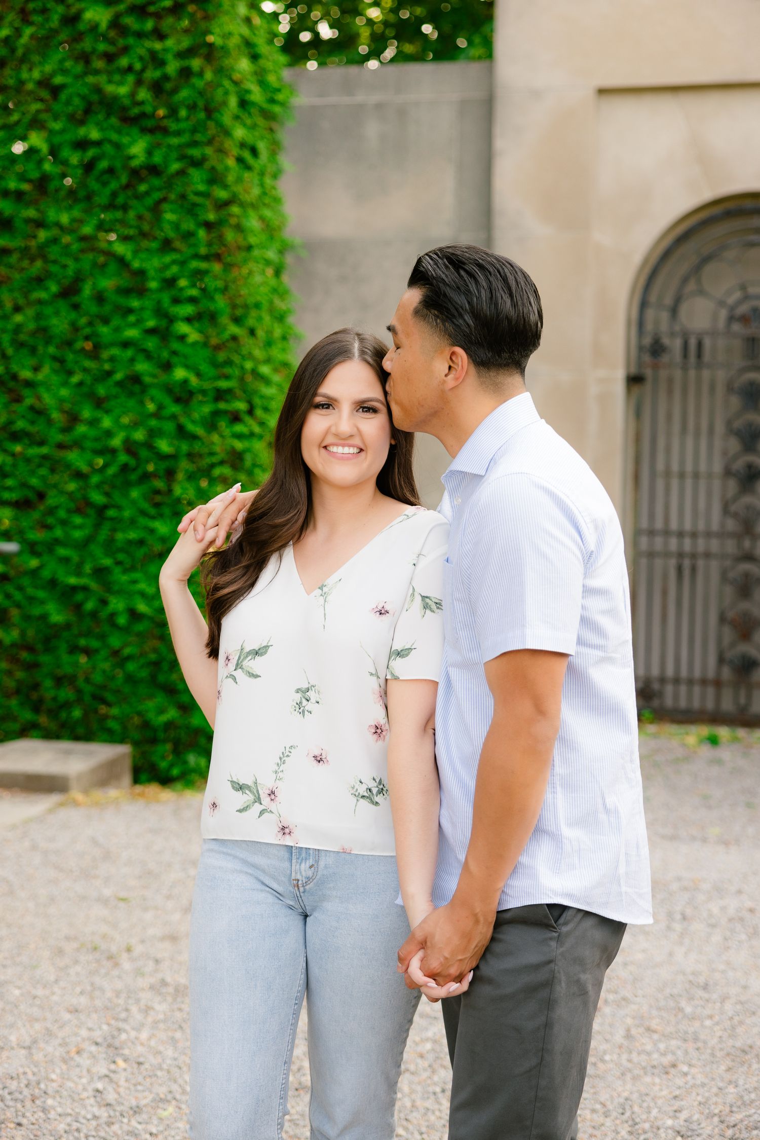 A romantic couple shares an intimate moment in front of a stone garden wall with climbing vines.