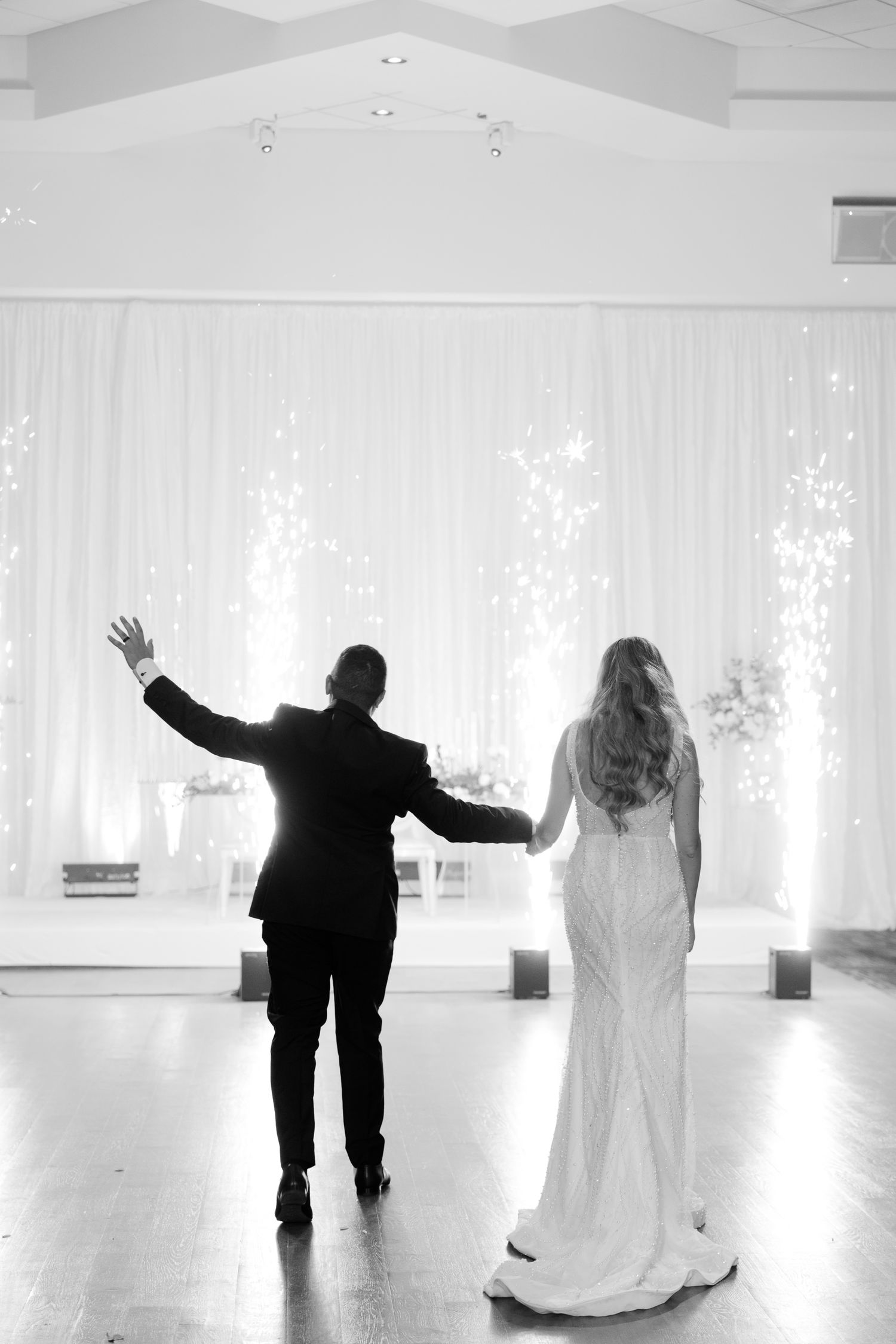 Black and white image of newlyweds walking with raised arms against a backdrop of sparklers.