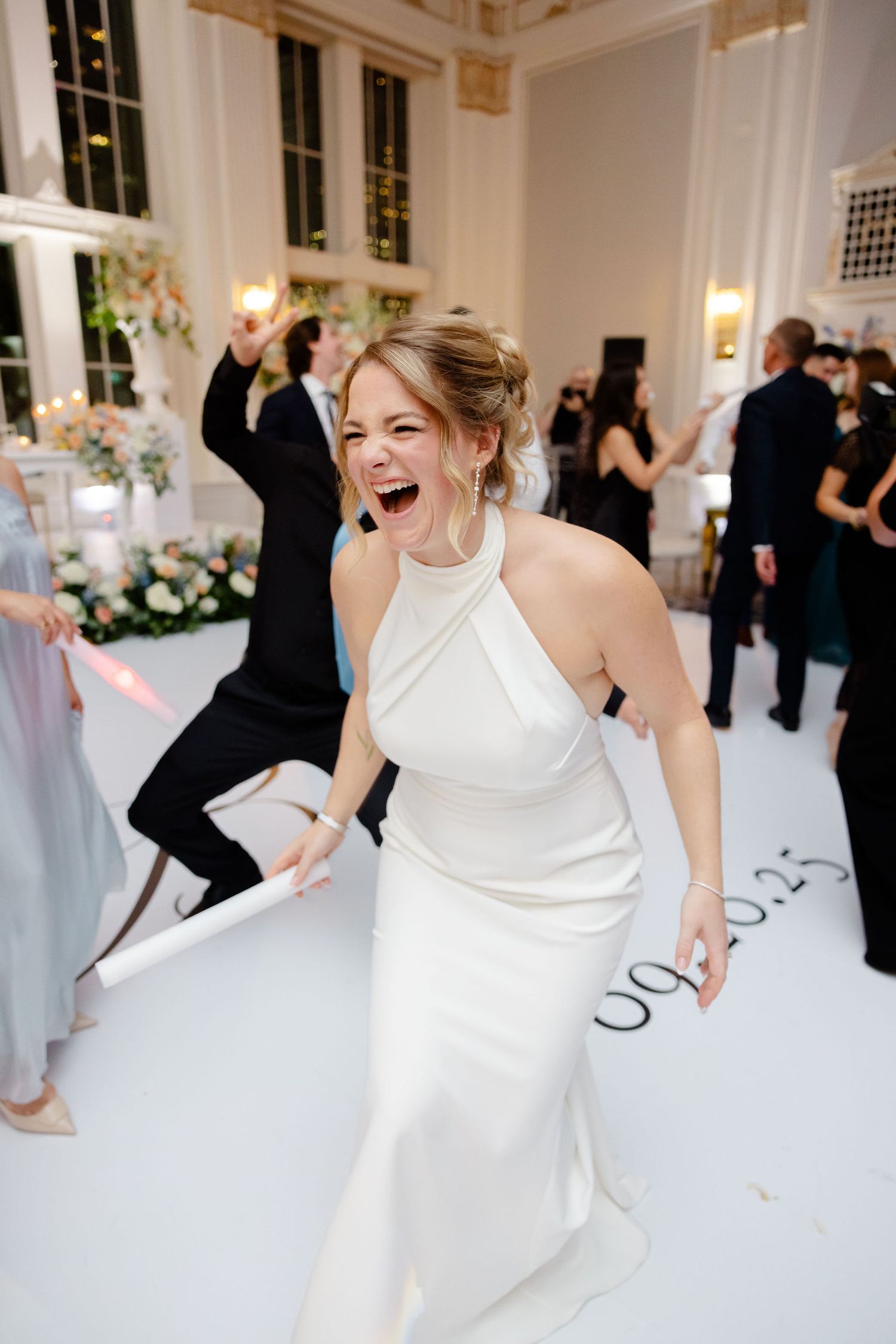 Joyful dancing sequence at a wedding reception in an elegant white ballroom with guests in the background.