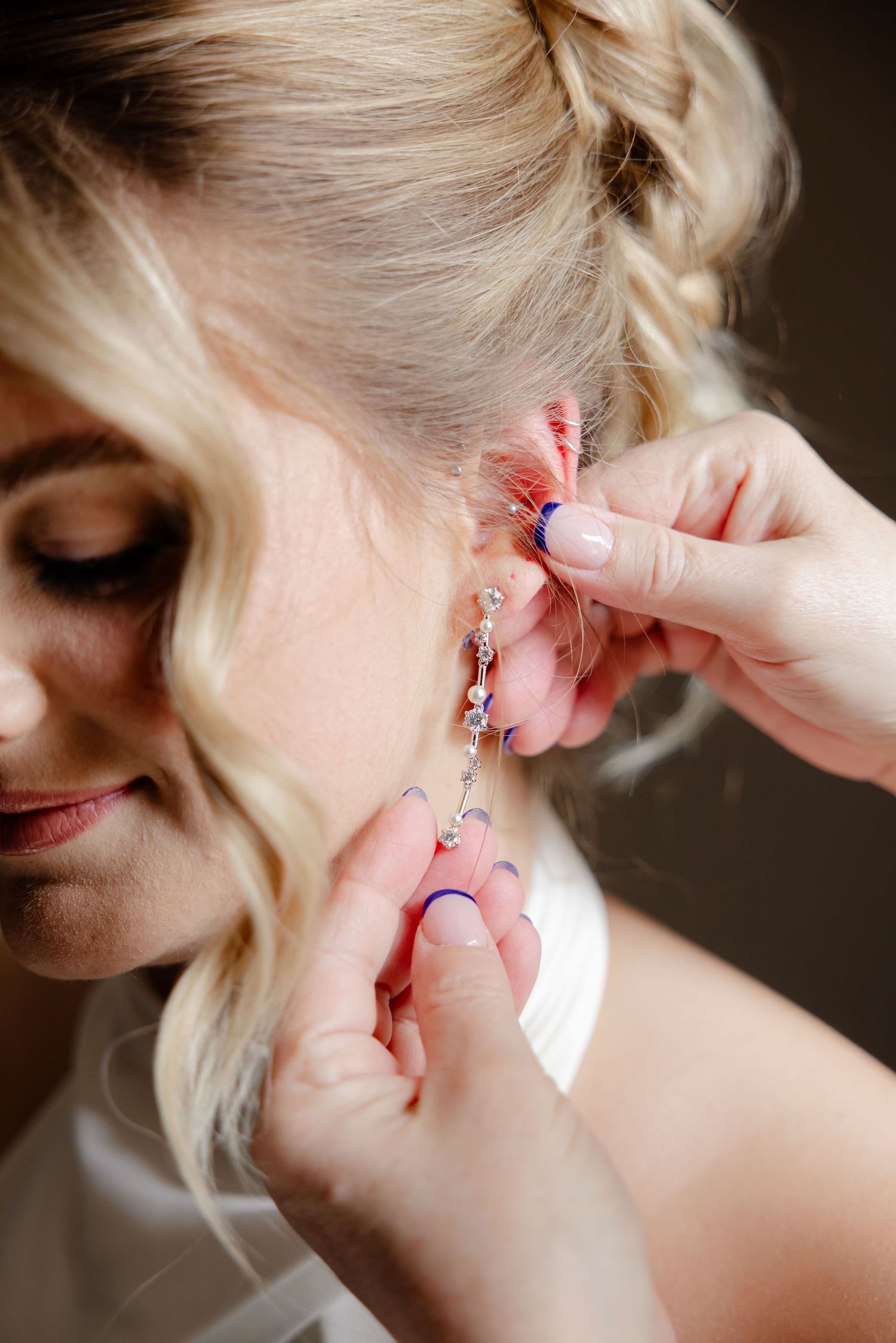 Close-up of hands putting on delicate earrings during wedding preparations.