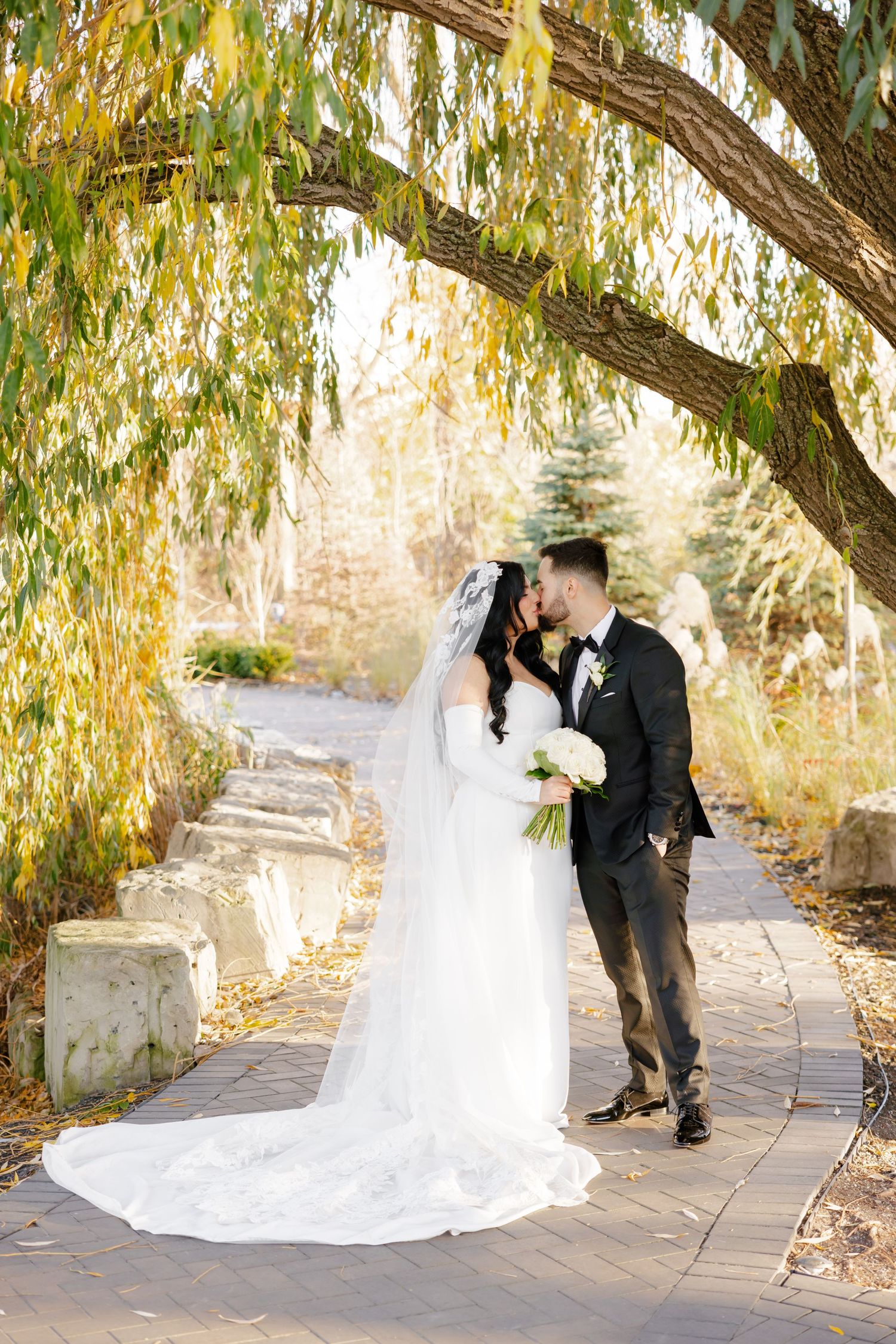 Romantic wedding couple shares intimate moment under golden willow branches.