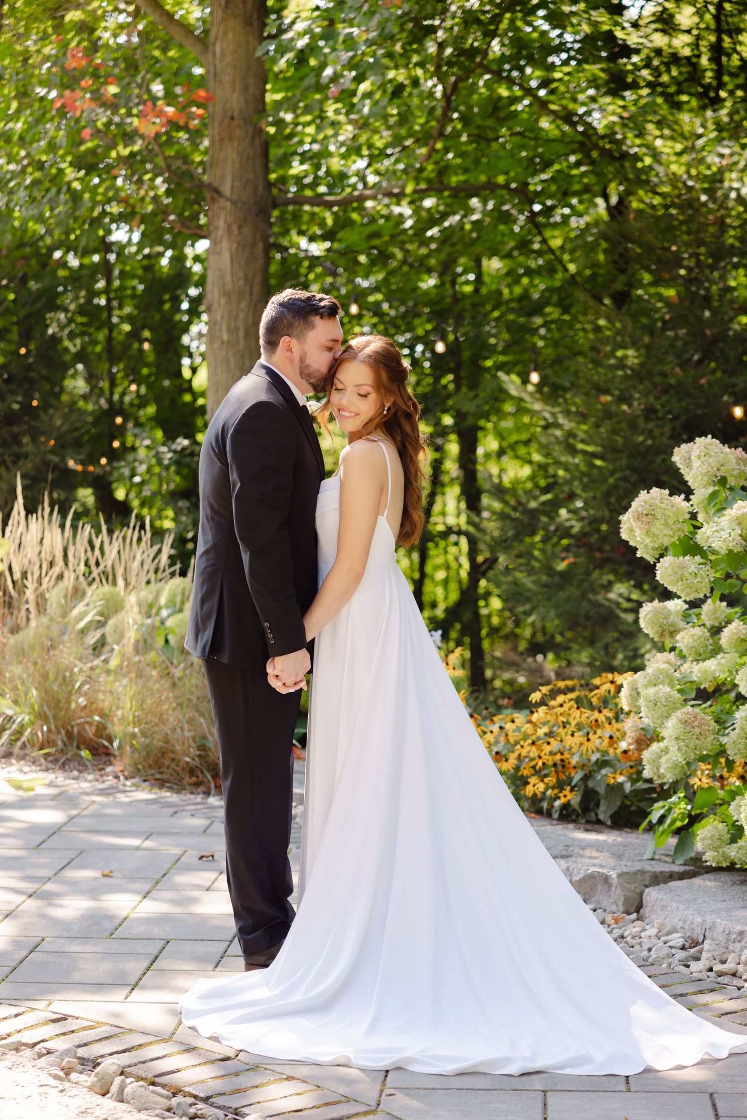 A tender moment between newlyweds on a garden path with flowering bushes and ornamental grasses.