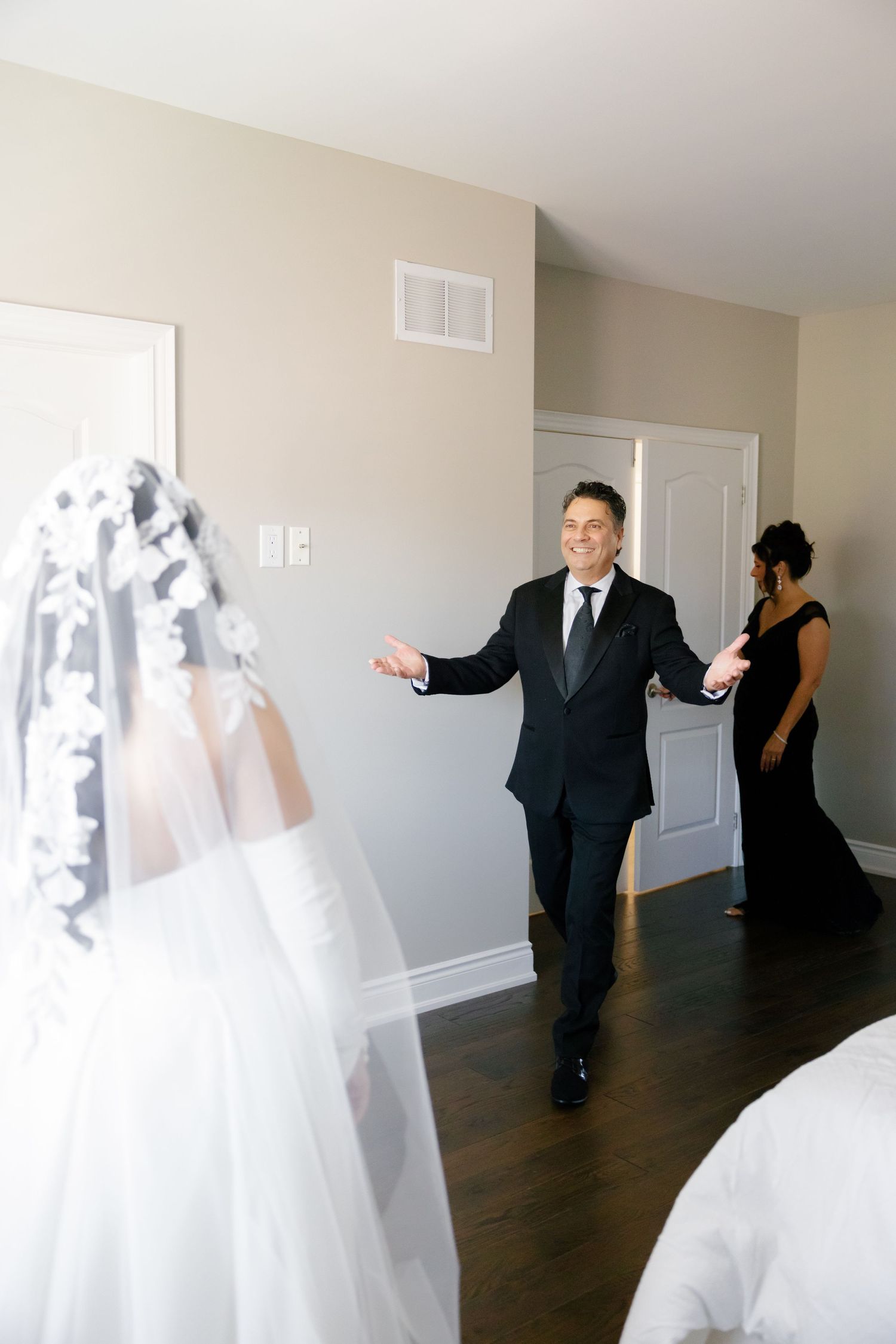 A wedding first look scene with groom in black suit entering the room.