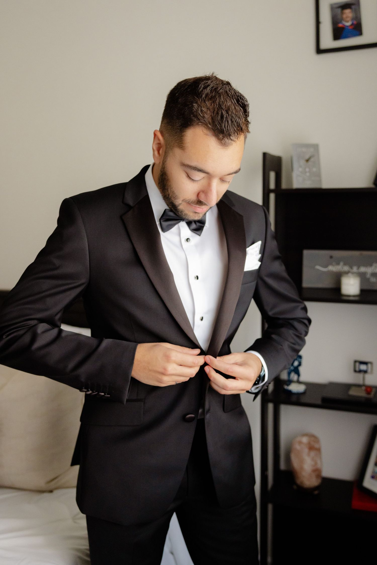 Groom adjusts buttons on formal black tuxedo jacket during wedding preparations.