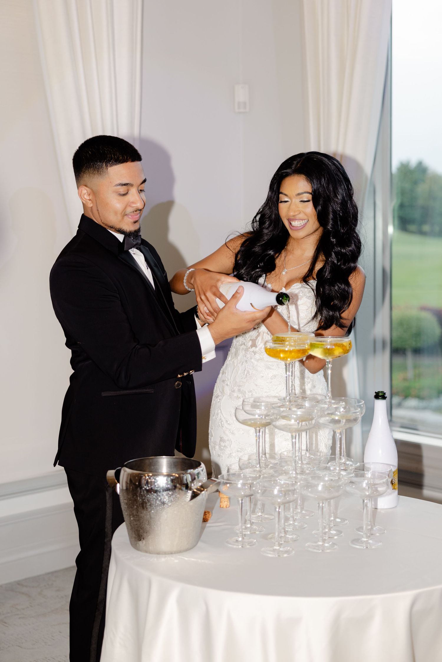 A couple pours champagne together into a tower of glasses at their wedding reception.